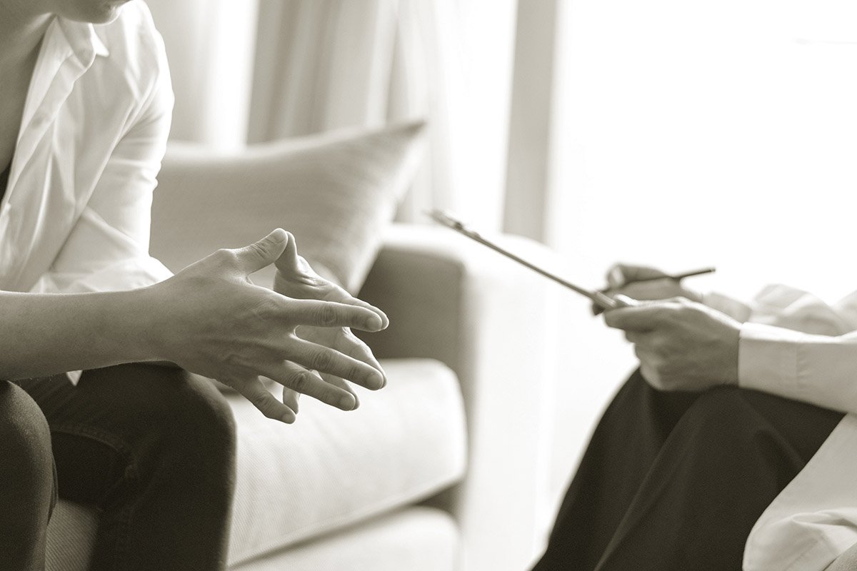 A person sitting on a couch talking to a therapist during a counseling session, with a therapist holding a notepad and pen.