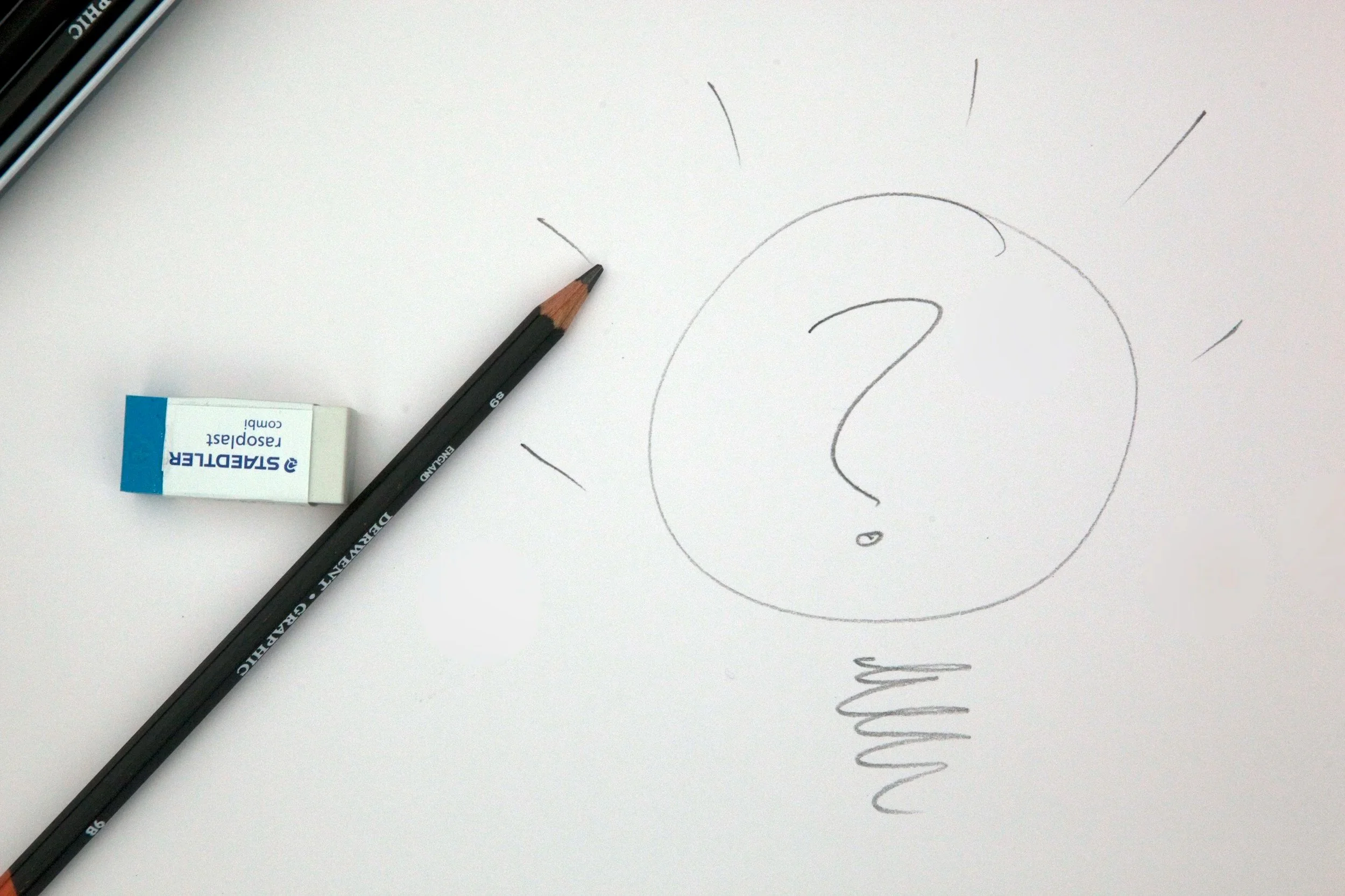 A sketch of a person's face with a large question mark in the middle of the page, a black pencil, and a white eraser.