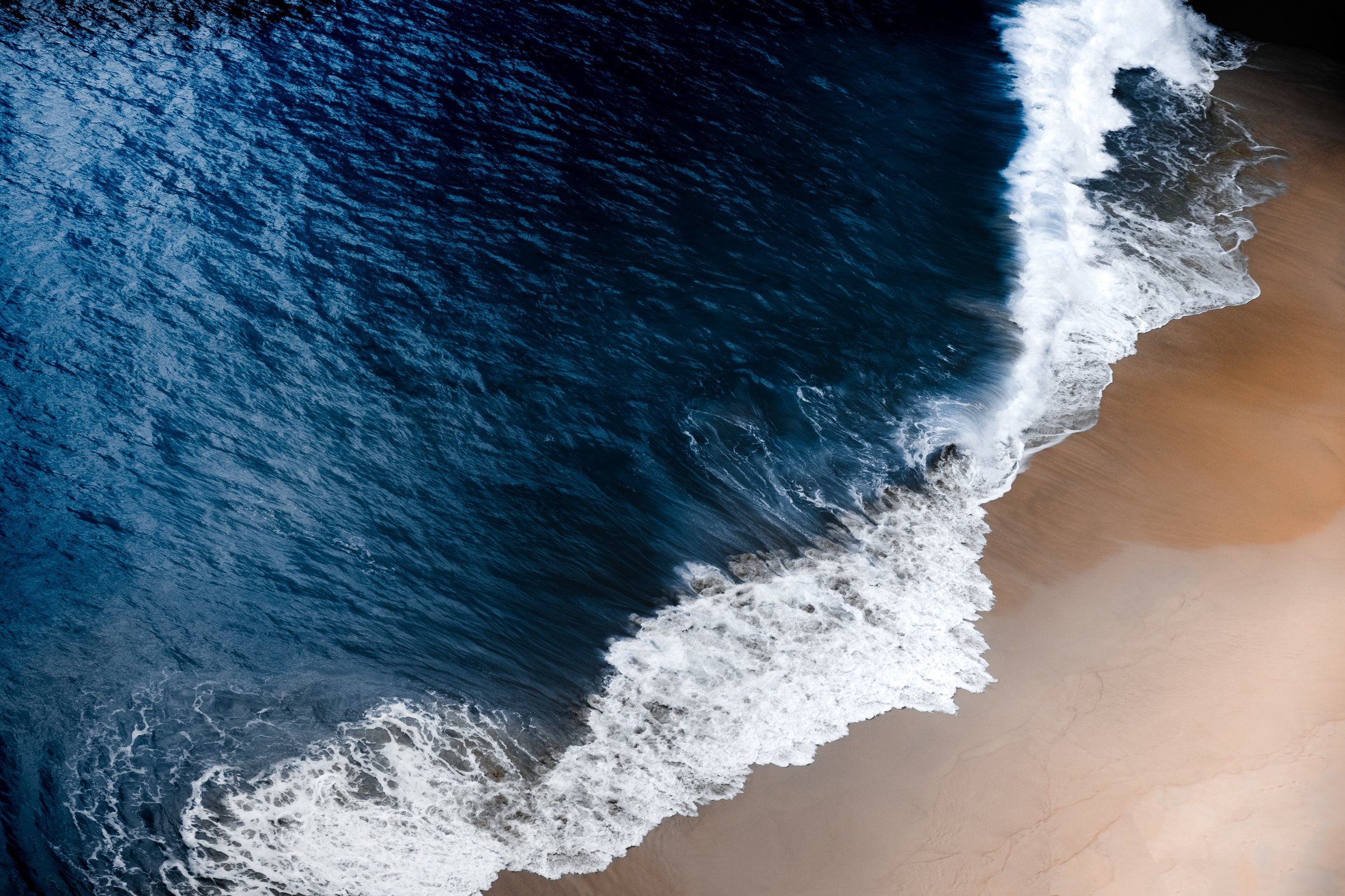 Ocean waves crashing onto sandy beach, viewed from above.