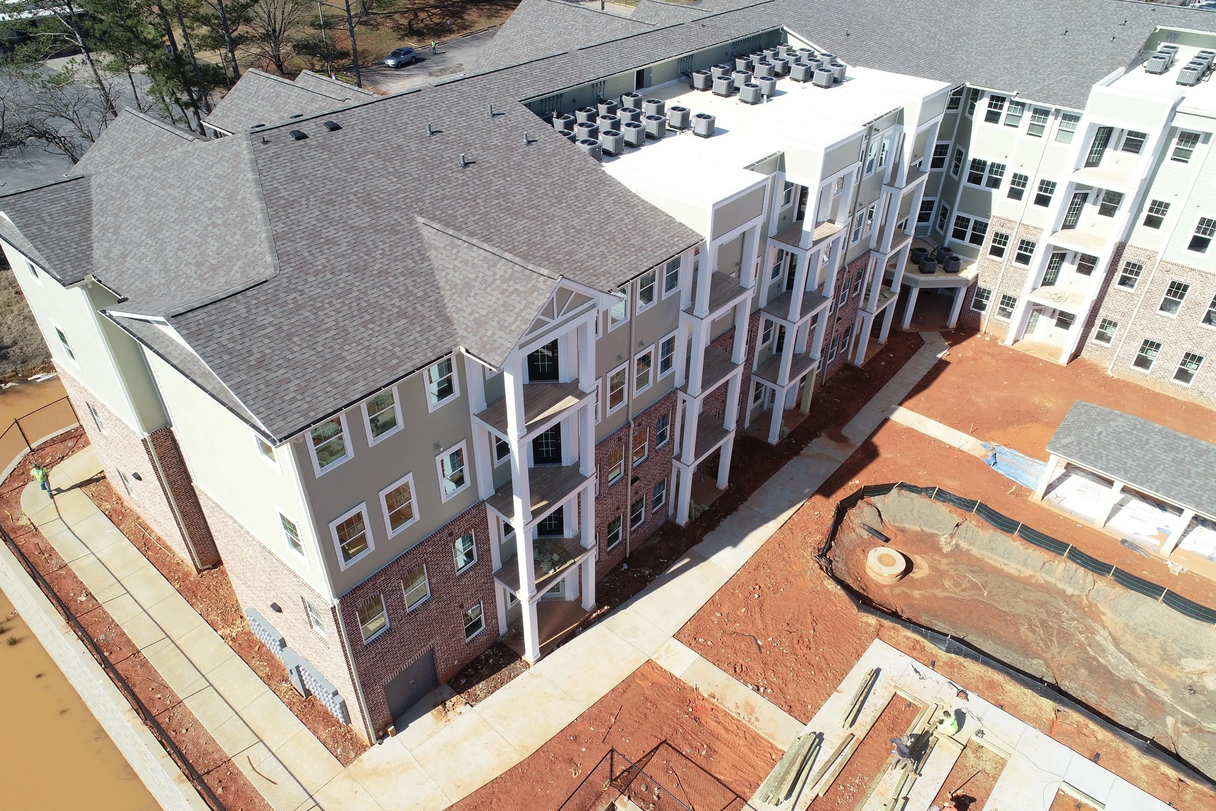 Aerial view of a multi-story residential building under construction, with external air conditioning units on the roof and construction materials on the ground.