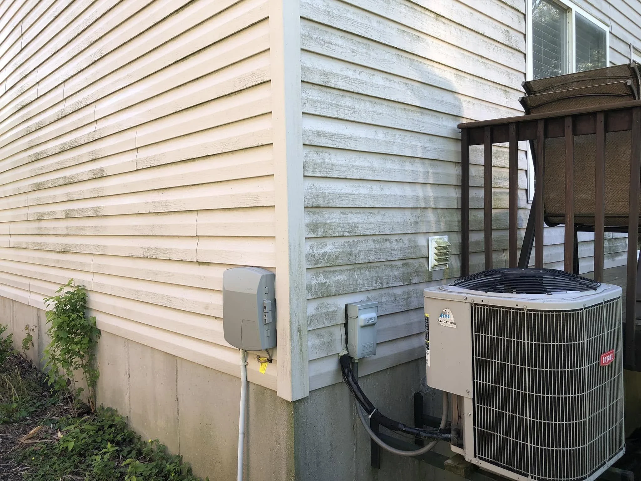 Exterior corner of a house showing beige horizontal vinyl siding, a window, an outdoor air conditioning unit, and an electrical box with conduit.