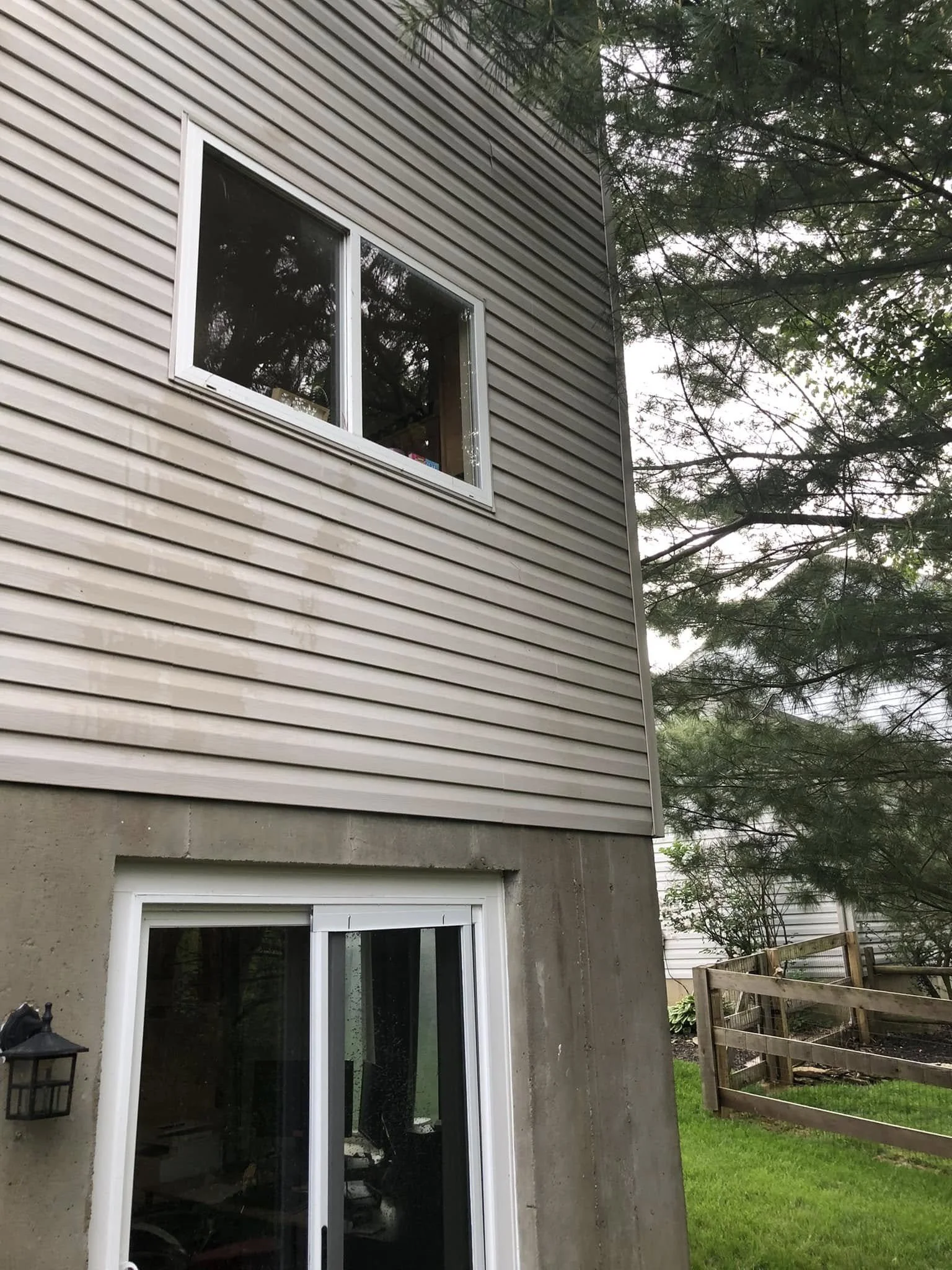 The image shows the exterior of a house with vinyl siding and a sliding glass door, with a backyard fence and trees in the background.