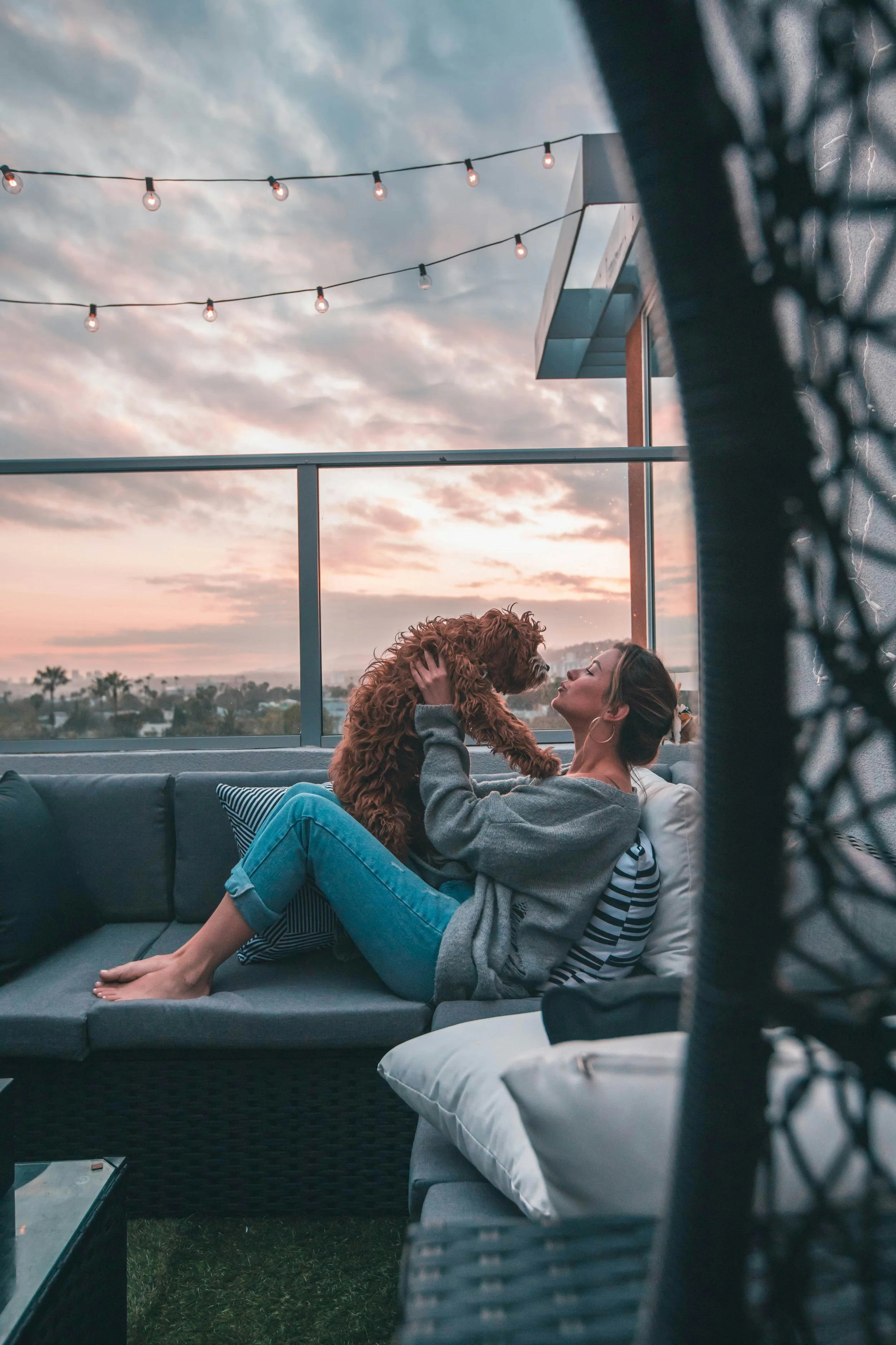 A woman and her dog sit on a rooftop patio enjoying sunset.