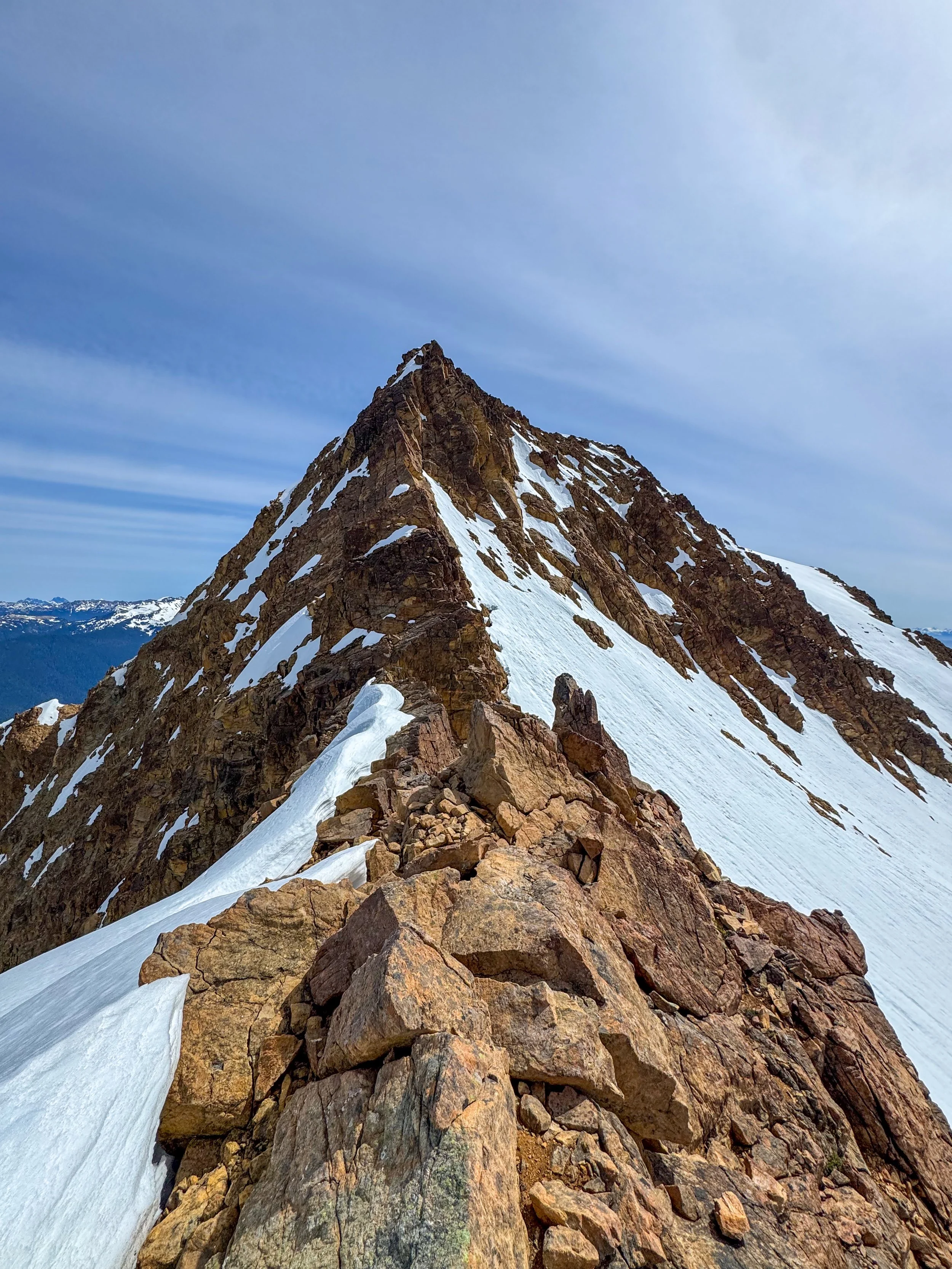 Snow-covered rocky mountain peak under a partly cloudy sky during daytime.