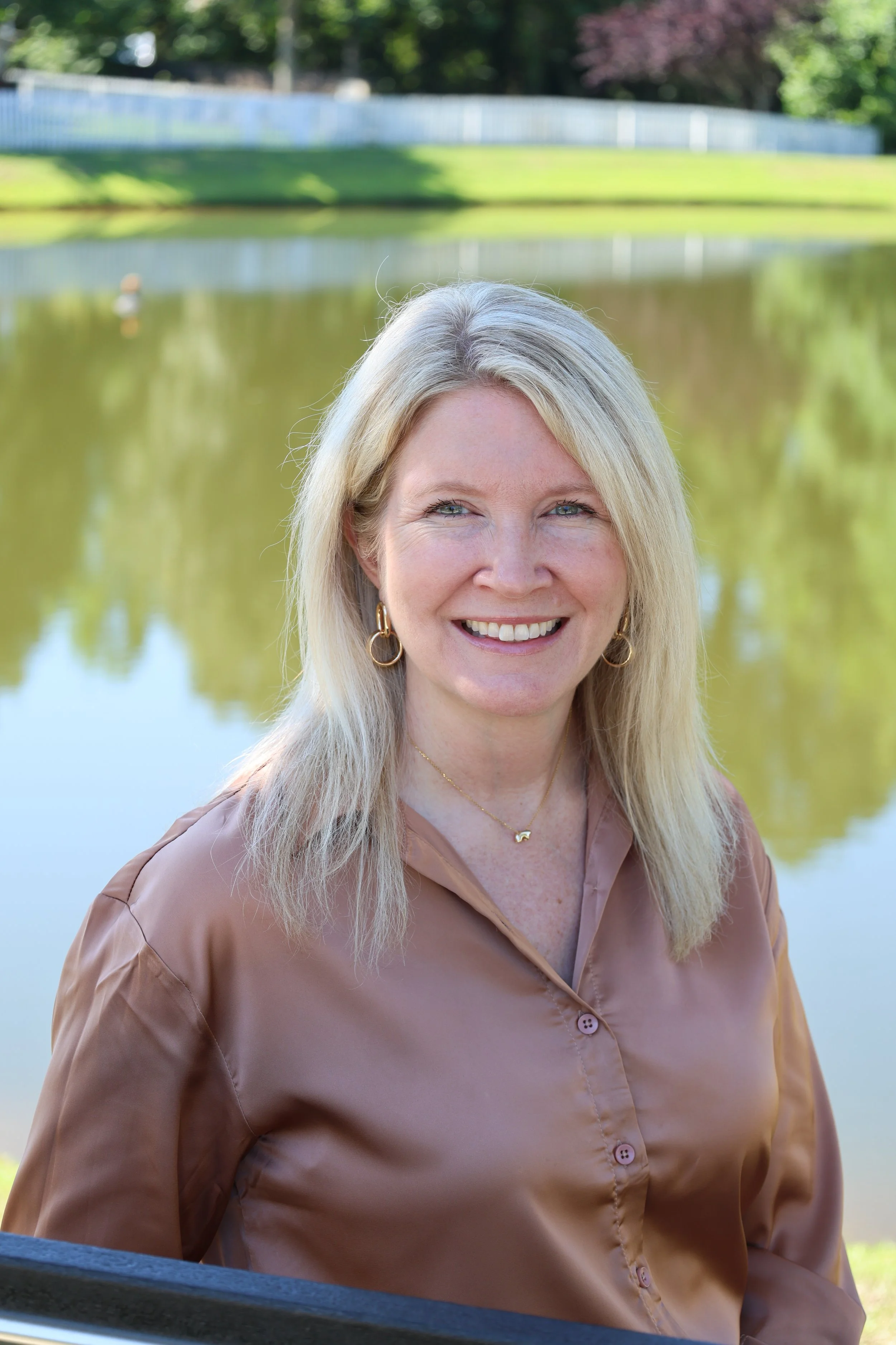Dana Santerre sitting peacefully on a bench by the pond, practicing presence and stillness