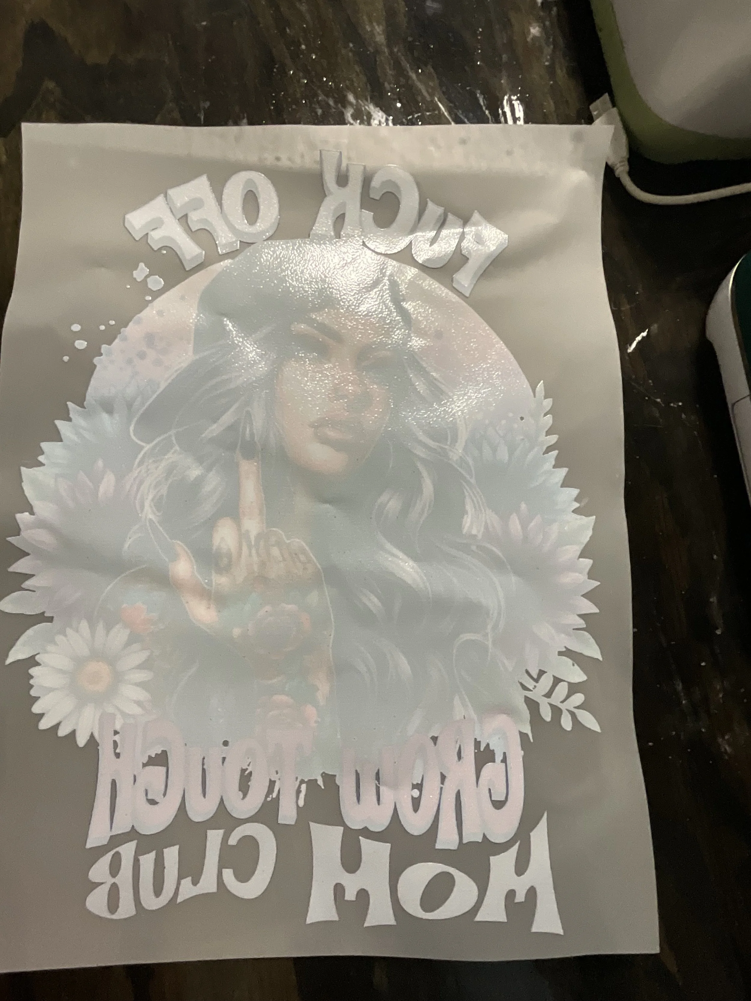 White sheet with text and images that are not clearly visible due to reflection, placed on a dark surface with an electrical cord and part of a bag visible