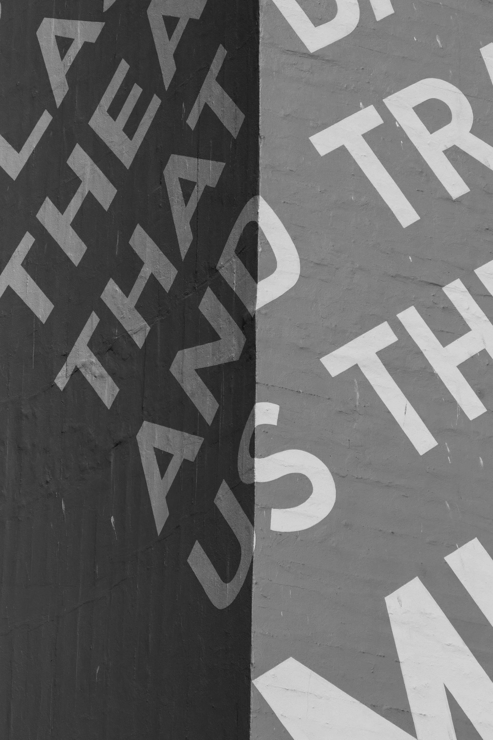 Black and white mural with overlapping word 'TRUST' on a brick wall.