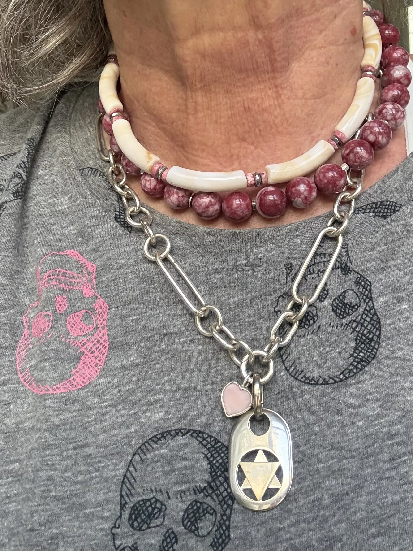 A person wearing layered necklaces with beads and charms, and a gray shirt with colorful skull prints.