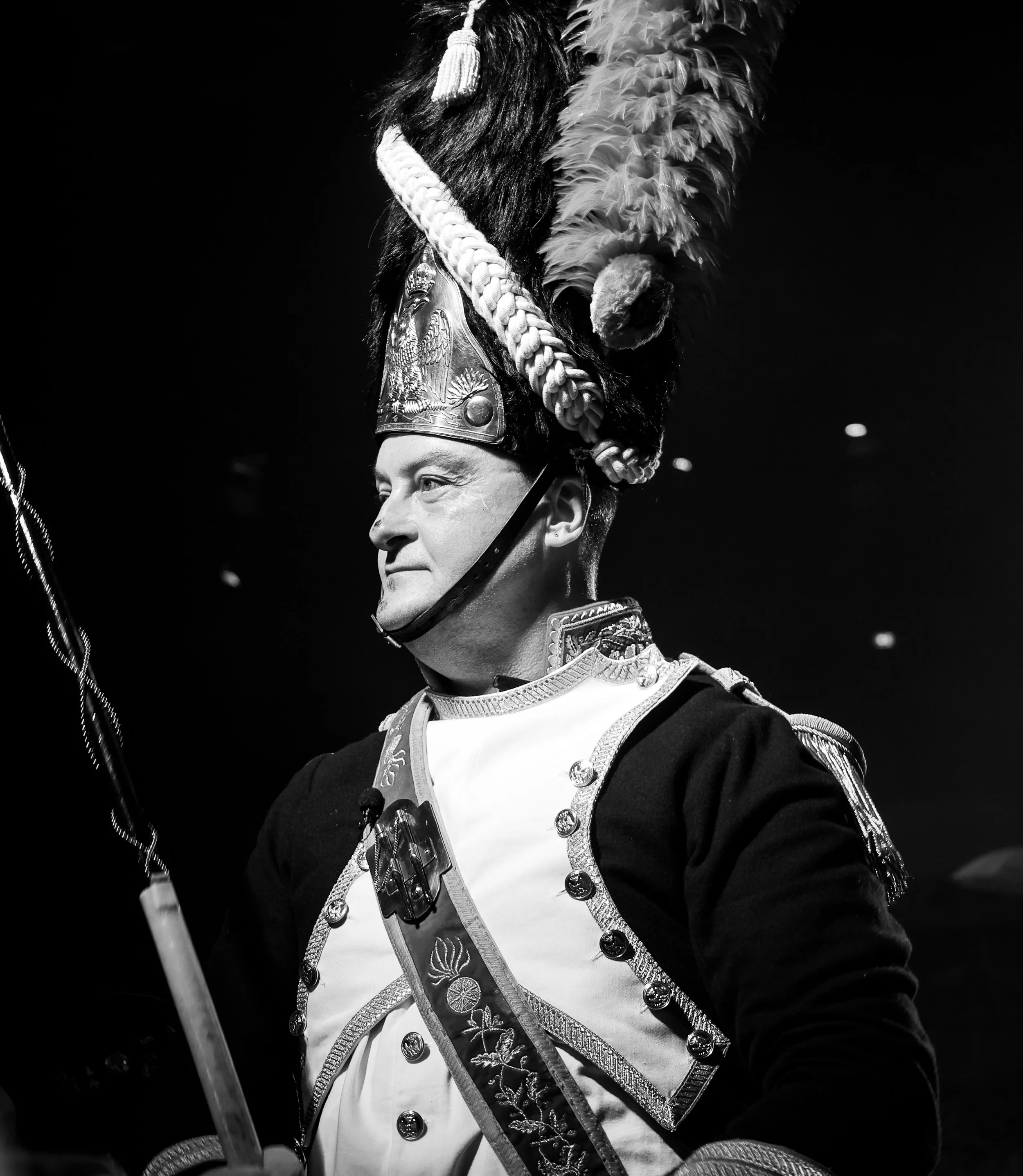 Uniforme de cérémonie d'un soldat en habit militaire avec chapeau orné de plumes et de décorations, tenant un drapeau.