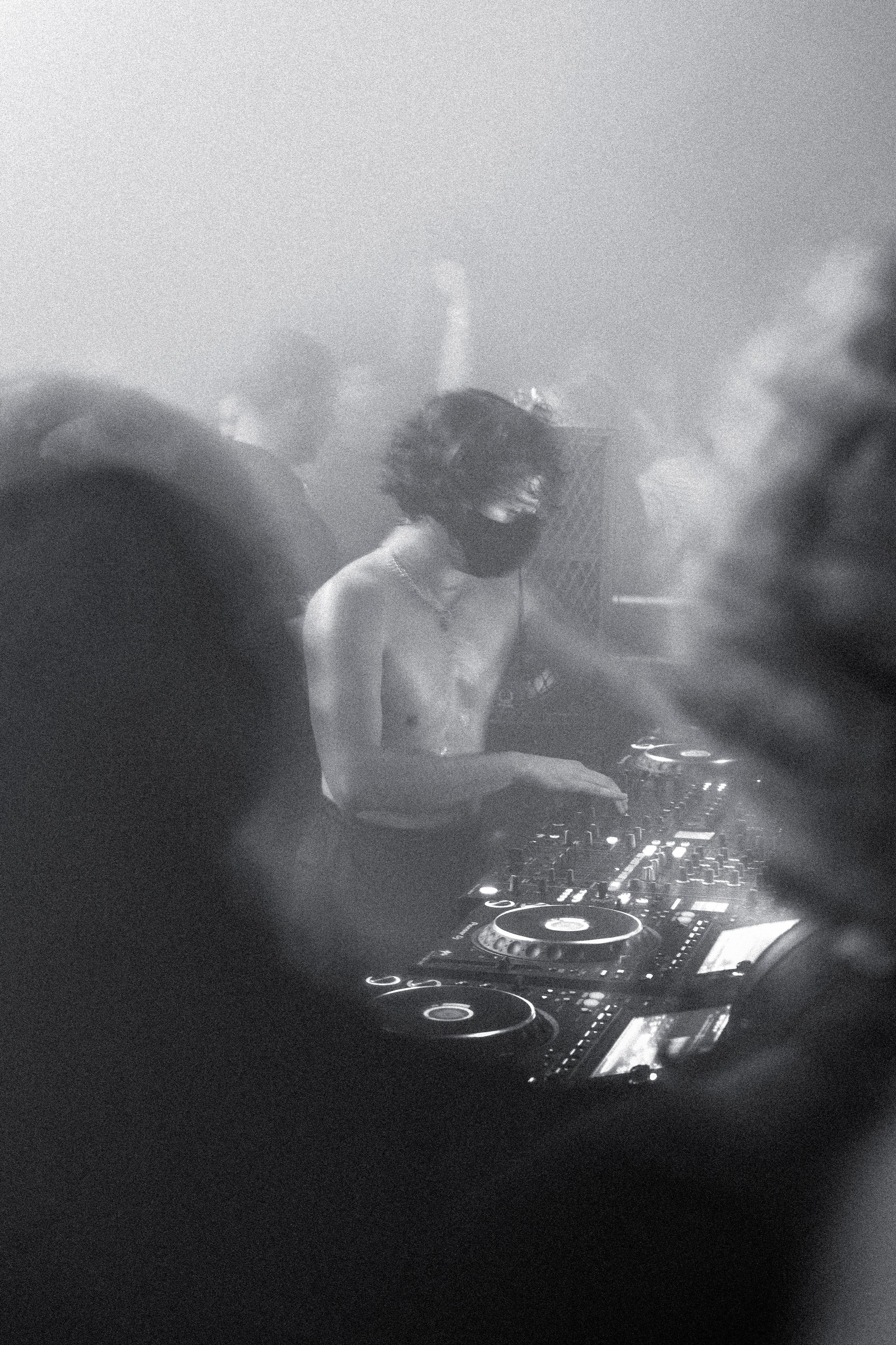 Un DJ mixant dans une boîte de nuit sombre, avec un casque audio et une console de DJ, entouré d'équipements lumineux.