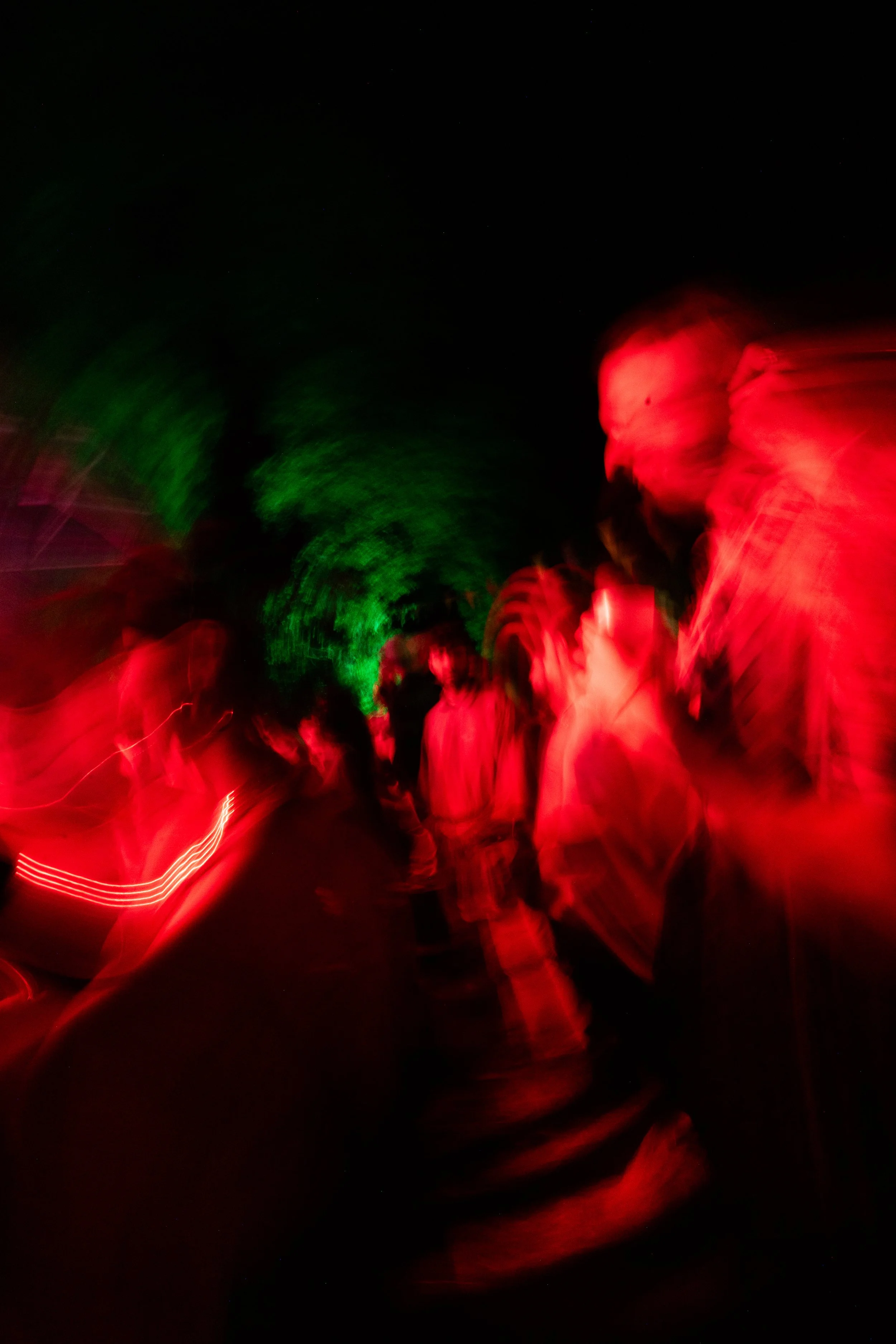Une scène nocturne avec des lumières rouges et vertes floues, présence de silhouettes humaines floues, création d'effets de mouvement et de lumière.