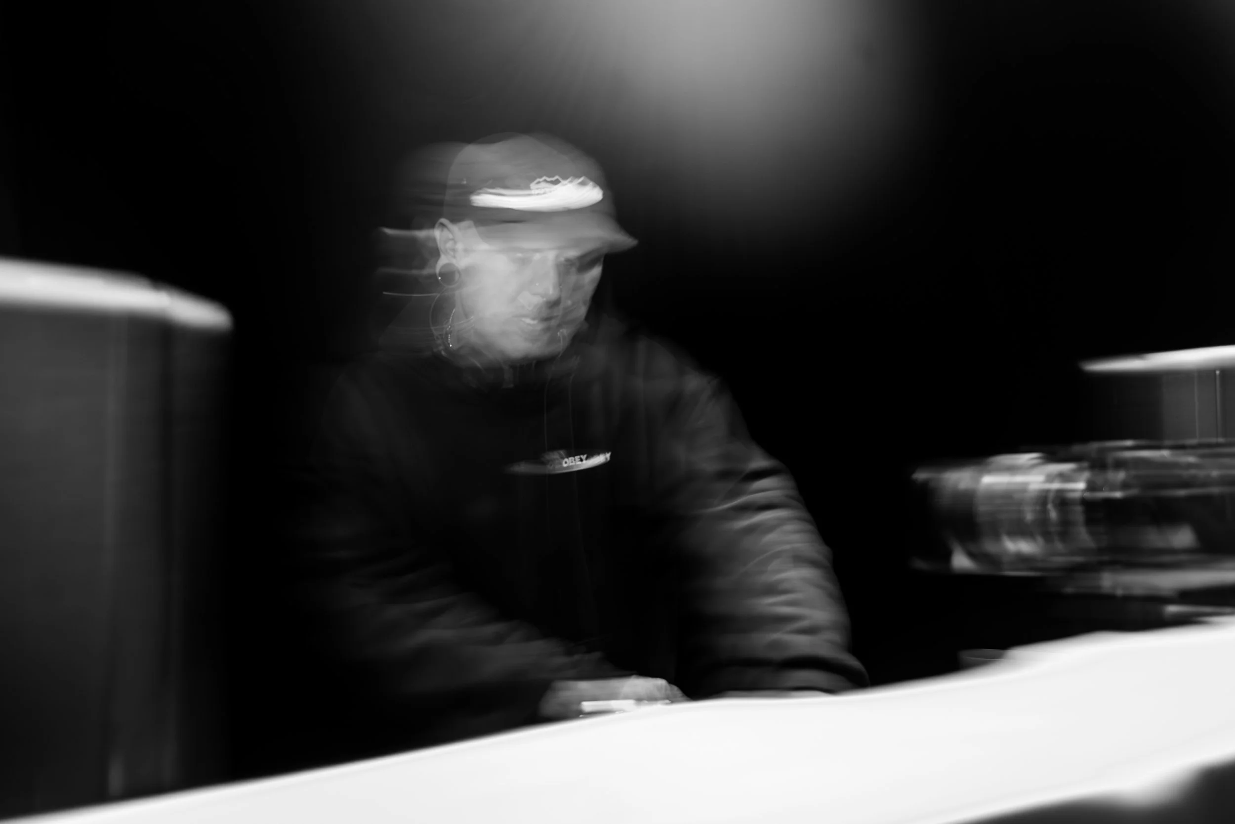 Une personne portant une casquette et des écouteurs, concentrée sur un clavier de piano électrique, dans un environnement sombre avec un éclairage ciblé