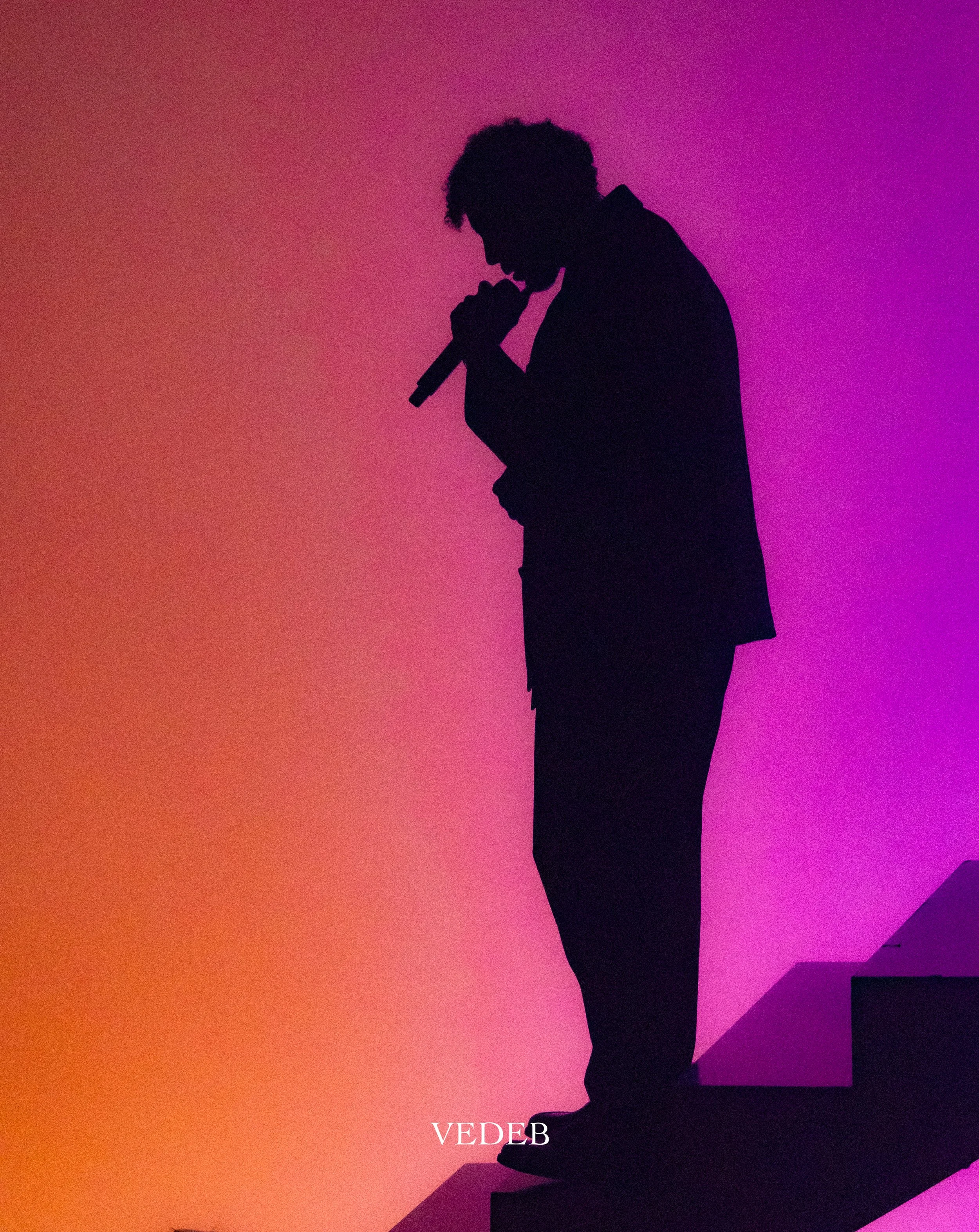 Silhouette d'un homme en noir se tenant debout, chapelet à la main, contre un fond dégradé de couleurs chaudes et froides, avec le texte 'VEDB' en bas.