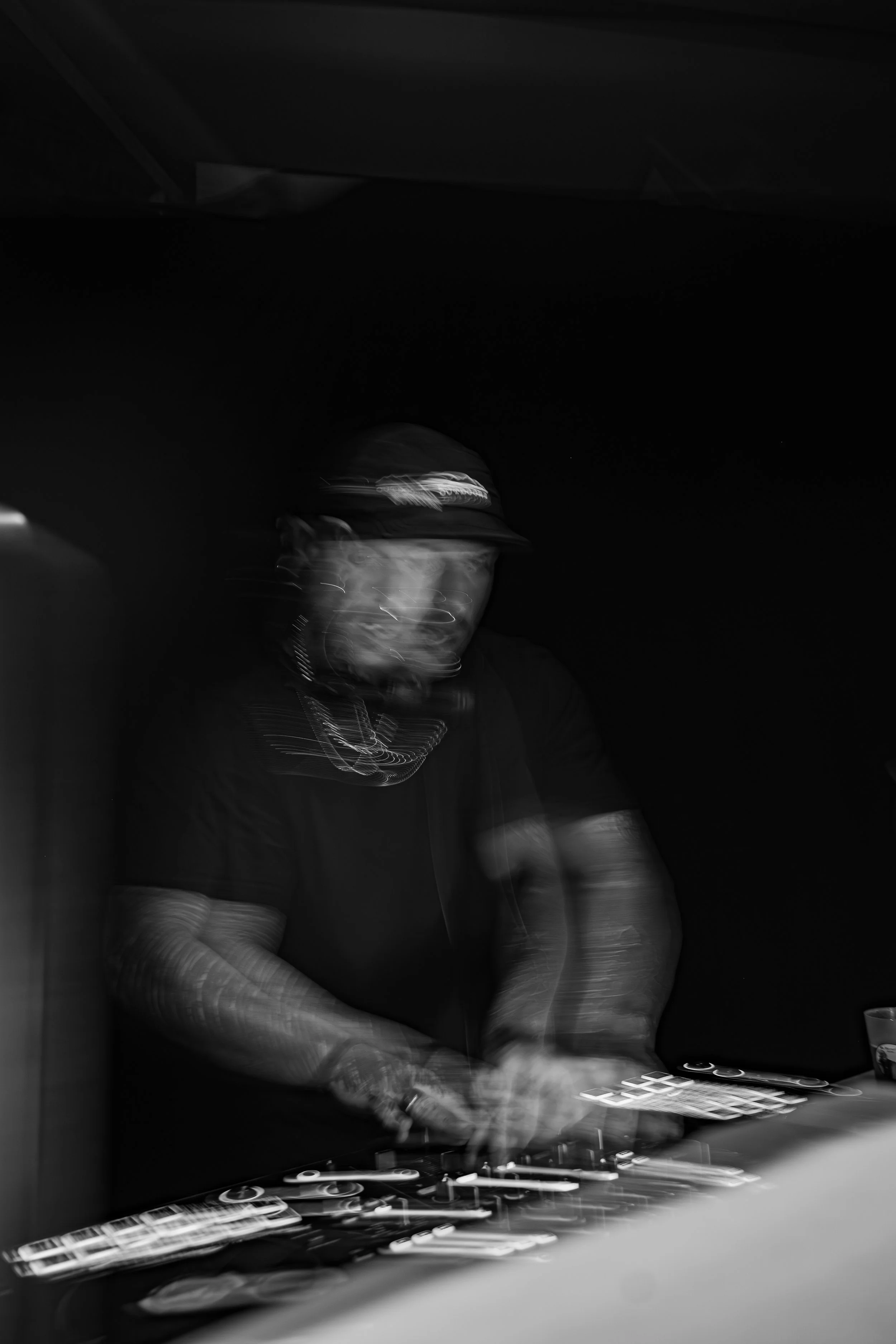 Une personne portant une casquette et des vêtements sombres, travaillant avec un équipement électronique ou numérique, dans un environnement sombre, avec un effet de mouvement dans l'image.