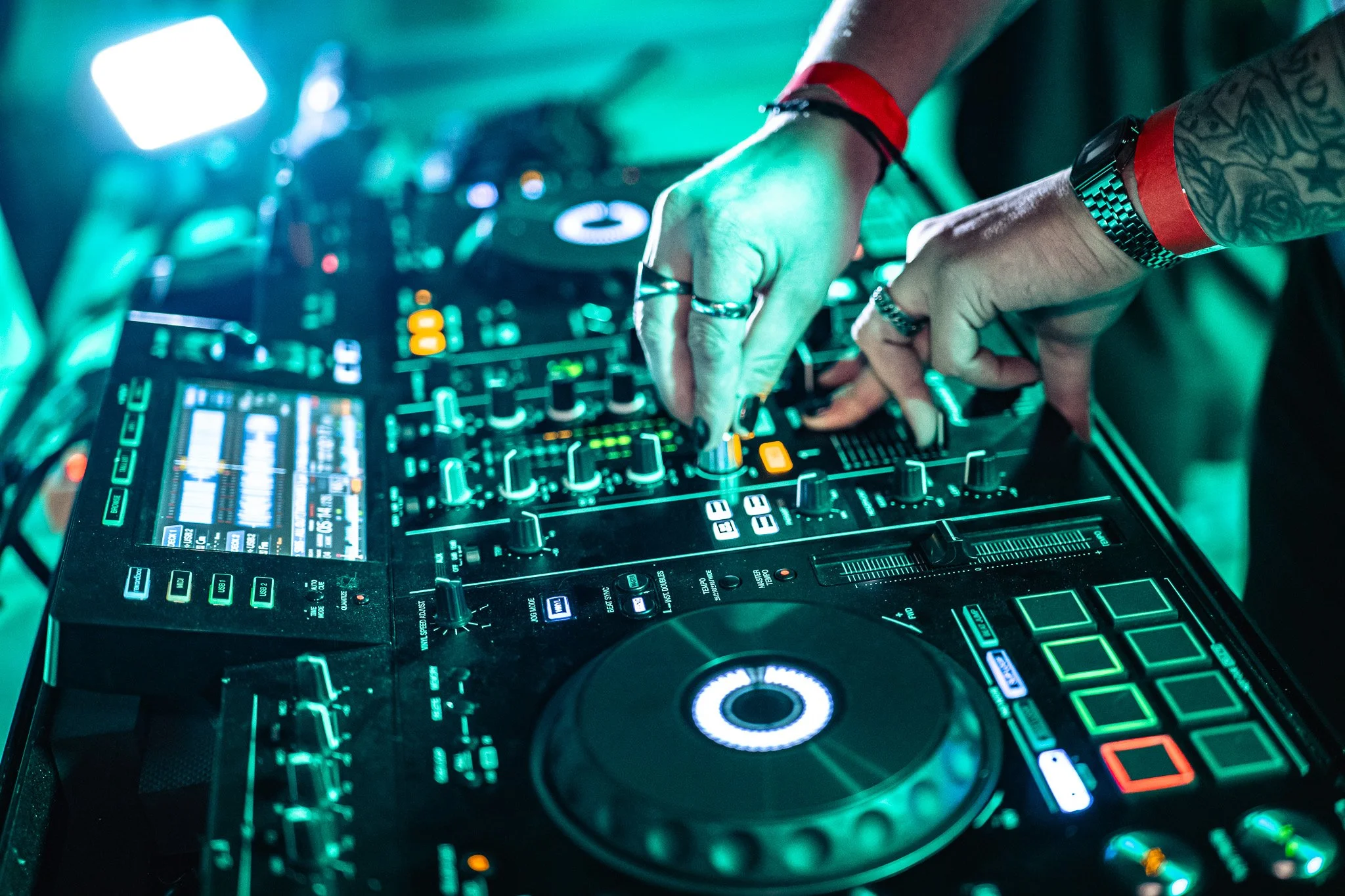 Un DJ manipulate des platines de musique avec des lumières multicolores dans une ambiance de fête ou de club.