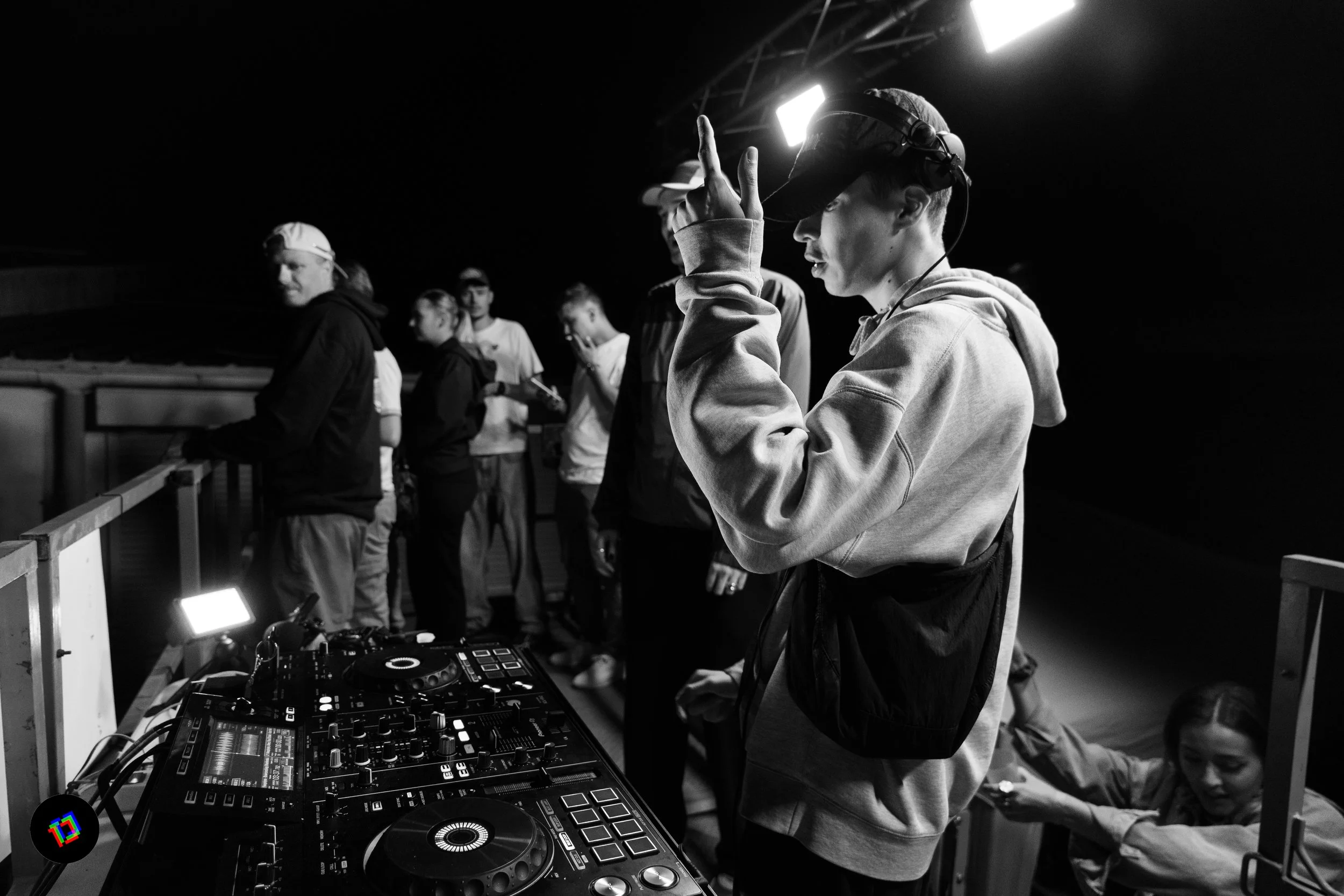 Un jeune DJ en train de mixer avec un casque lors d'une soirée en intérieur, entouré de plusieurs personnes.