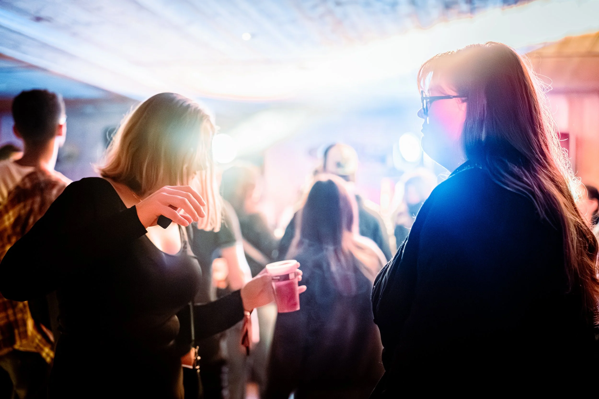 Groupe de jeunes femmes dans une ambiance colorée et lumineuse, socialisant lors d'une fête ou d'un événement intérieur.