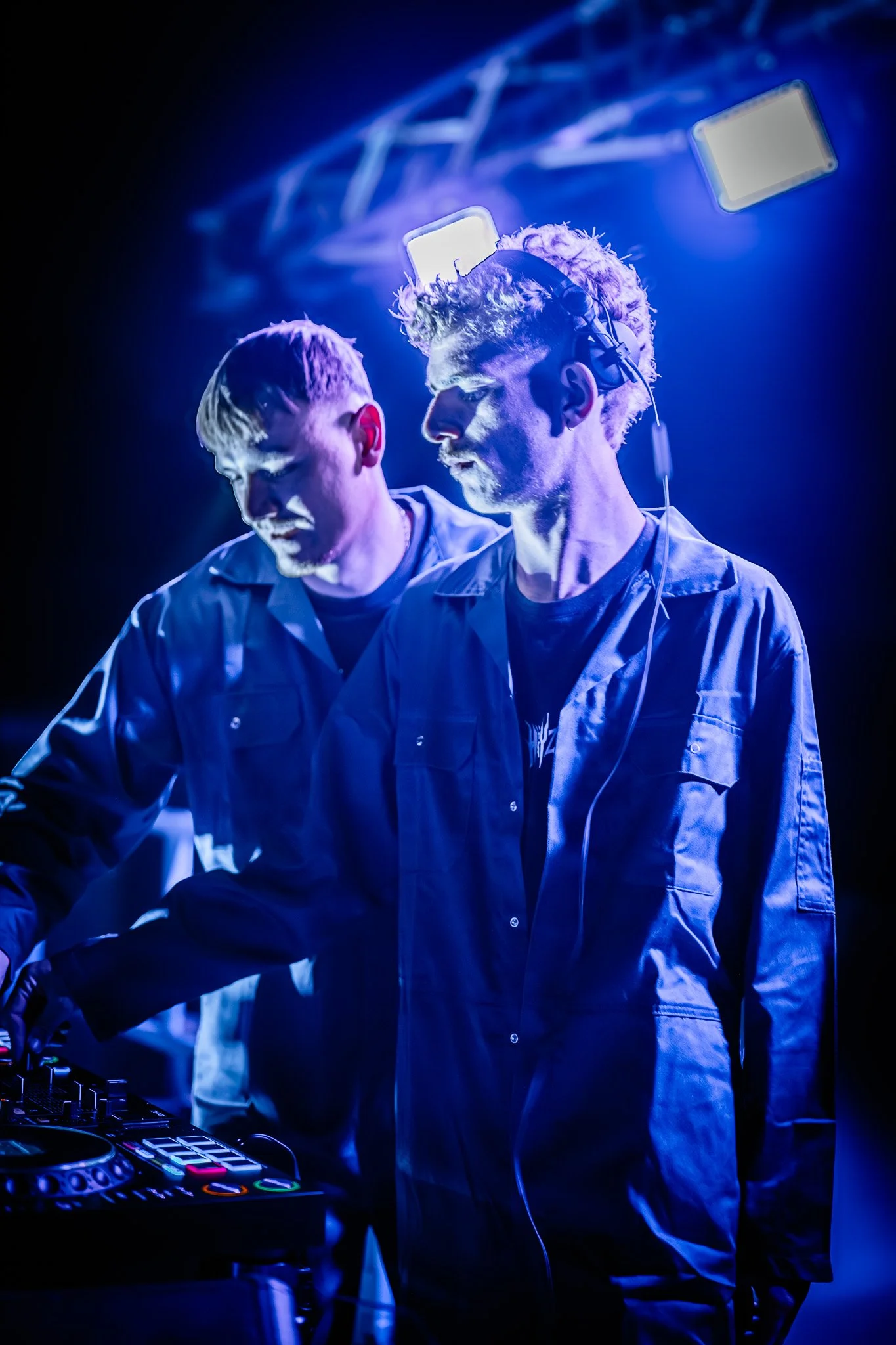 Deux DJ en train de mixer lors d'une performance, sous un éclairage bleu et violet, avec un casque un DJ portant des vêtements décontractés.