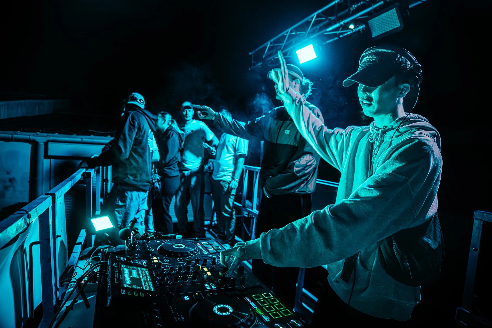DJ jouant de la musique lors d'une soirée en plein air avec un groupe de personnes, éclairé par des lumières bleues et tetesptes électroniques.