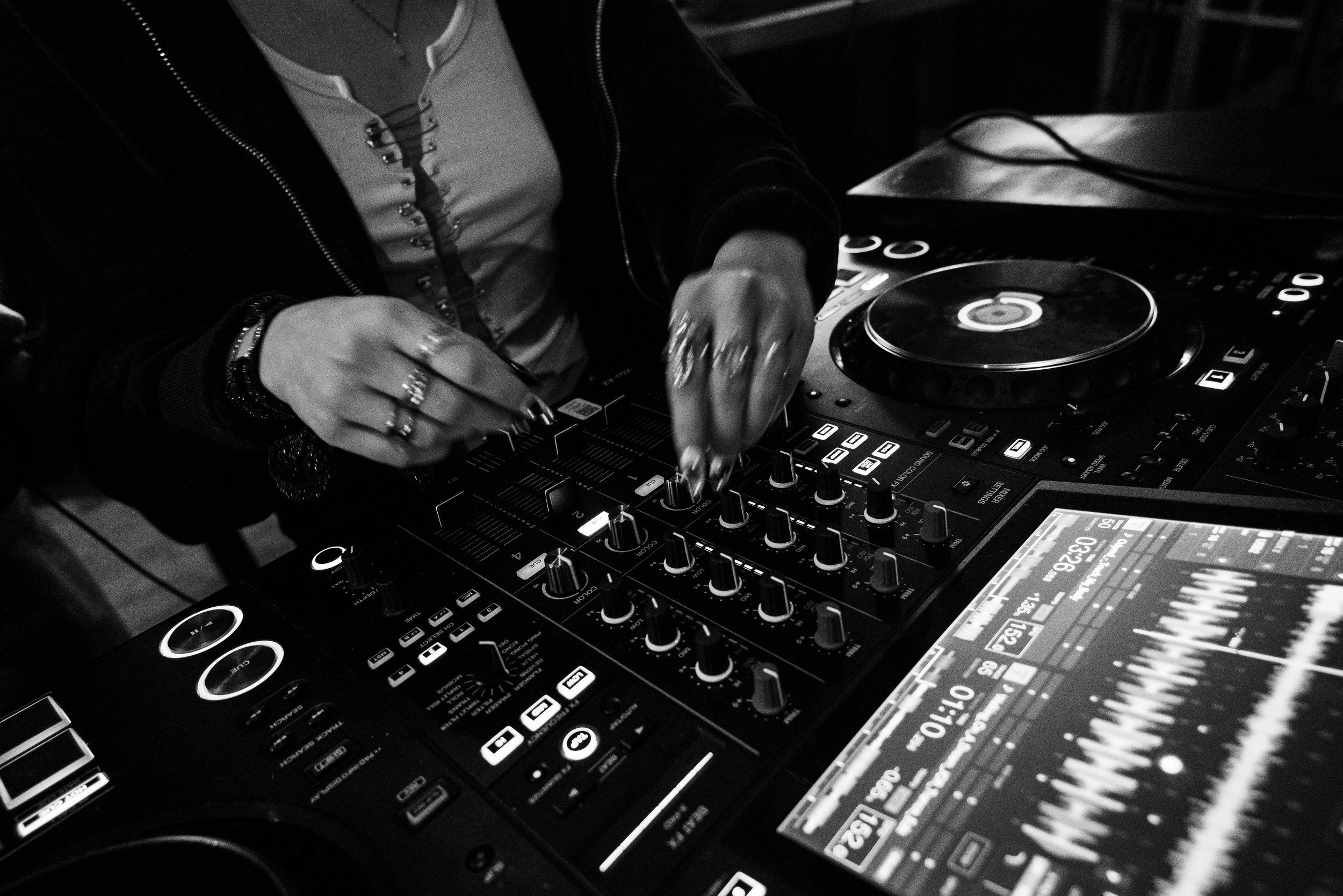 Un DJ manipule des commandes de mixage sur une console dans un environnement sombre. 