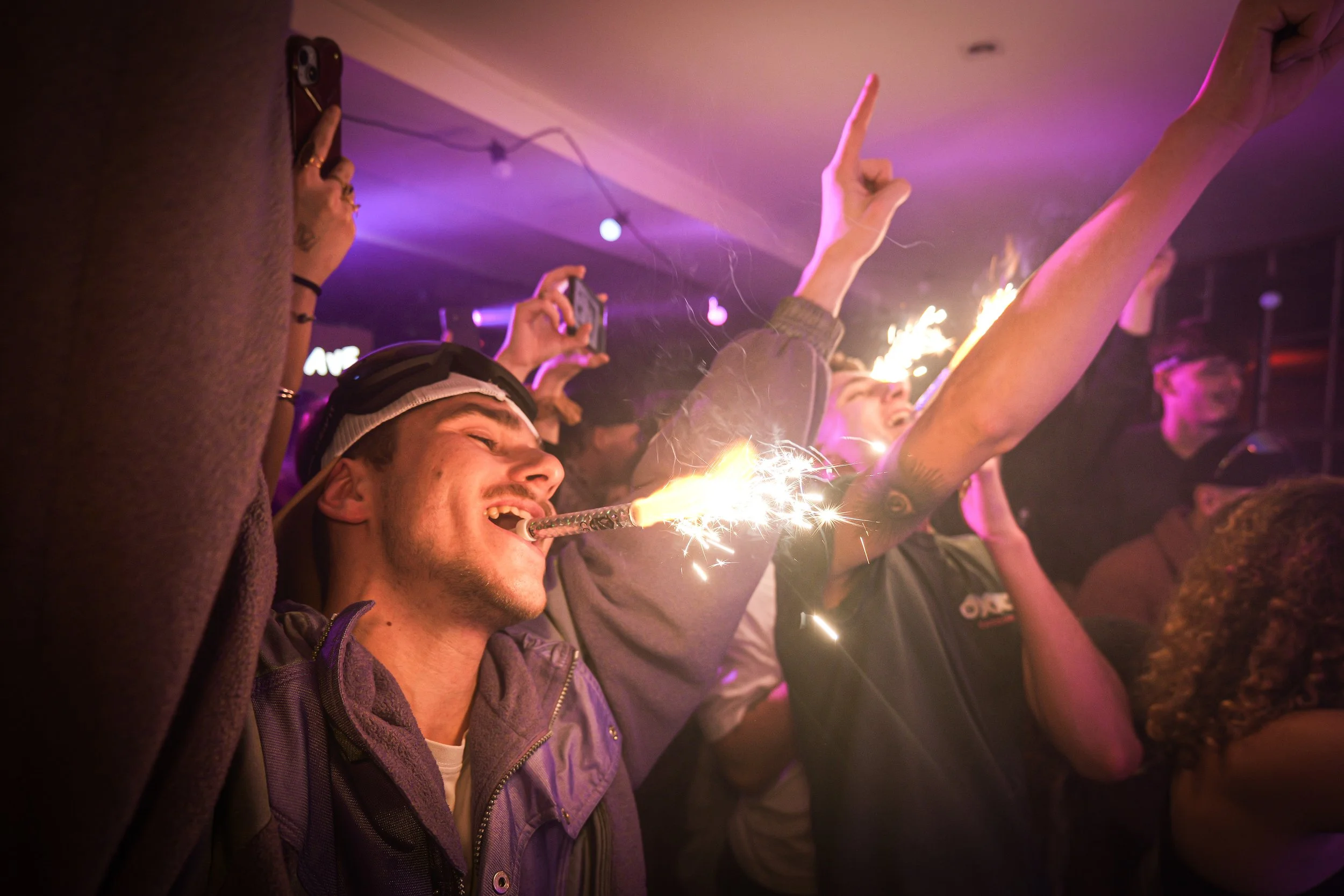 Groupe de jeunes à une fête, avec une personne qui a un lanceur de feux d'artifice ou un pétard, dans une ambiance animée.
