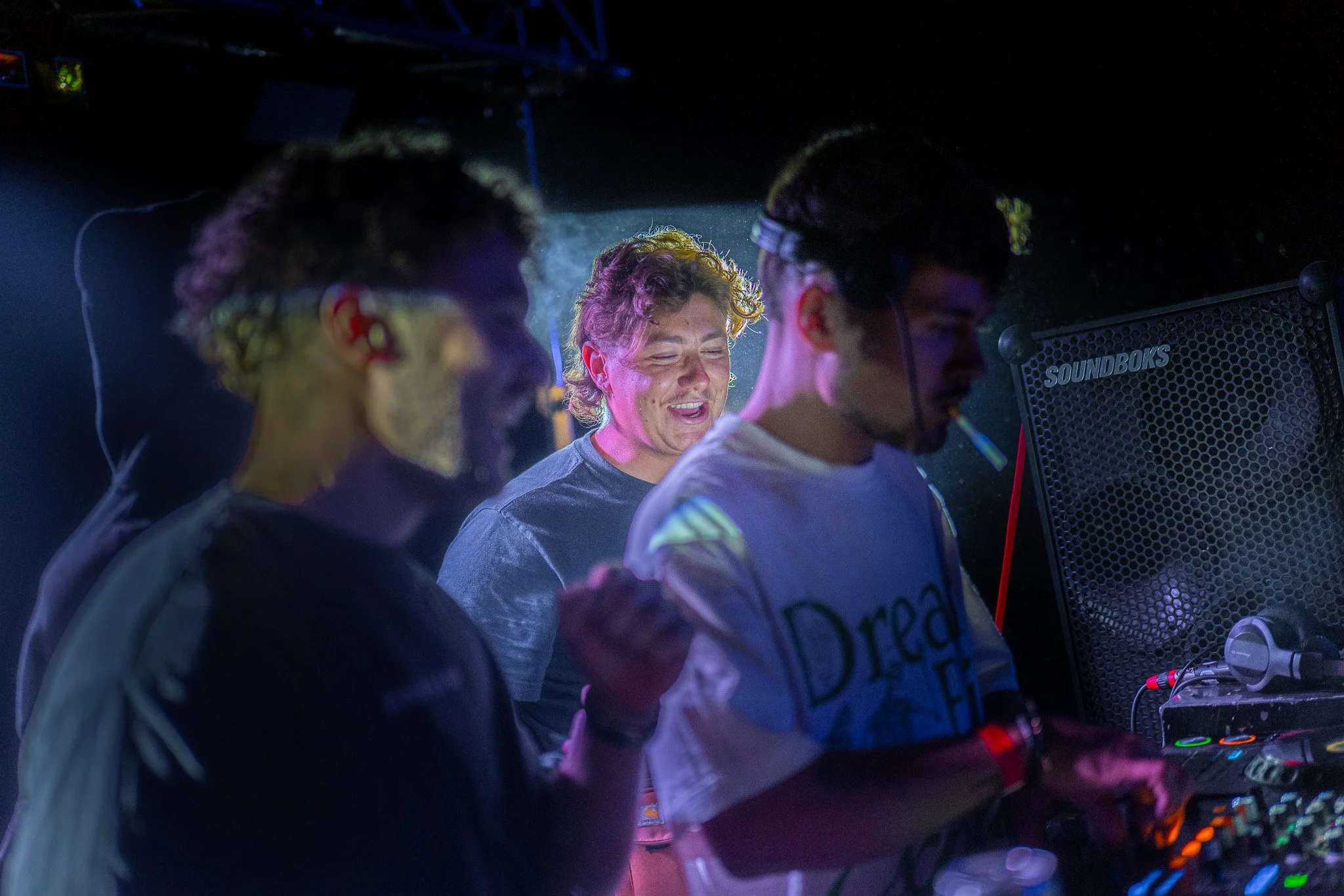 Groupe de personnes DJ en boîte de nuit, lumières colorées, écran de son, ambiance festive.