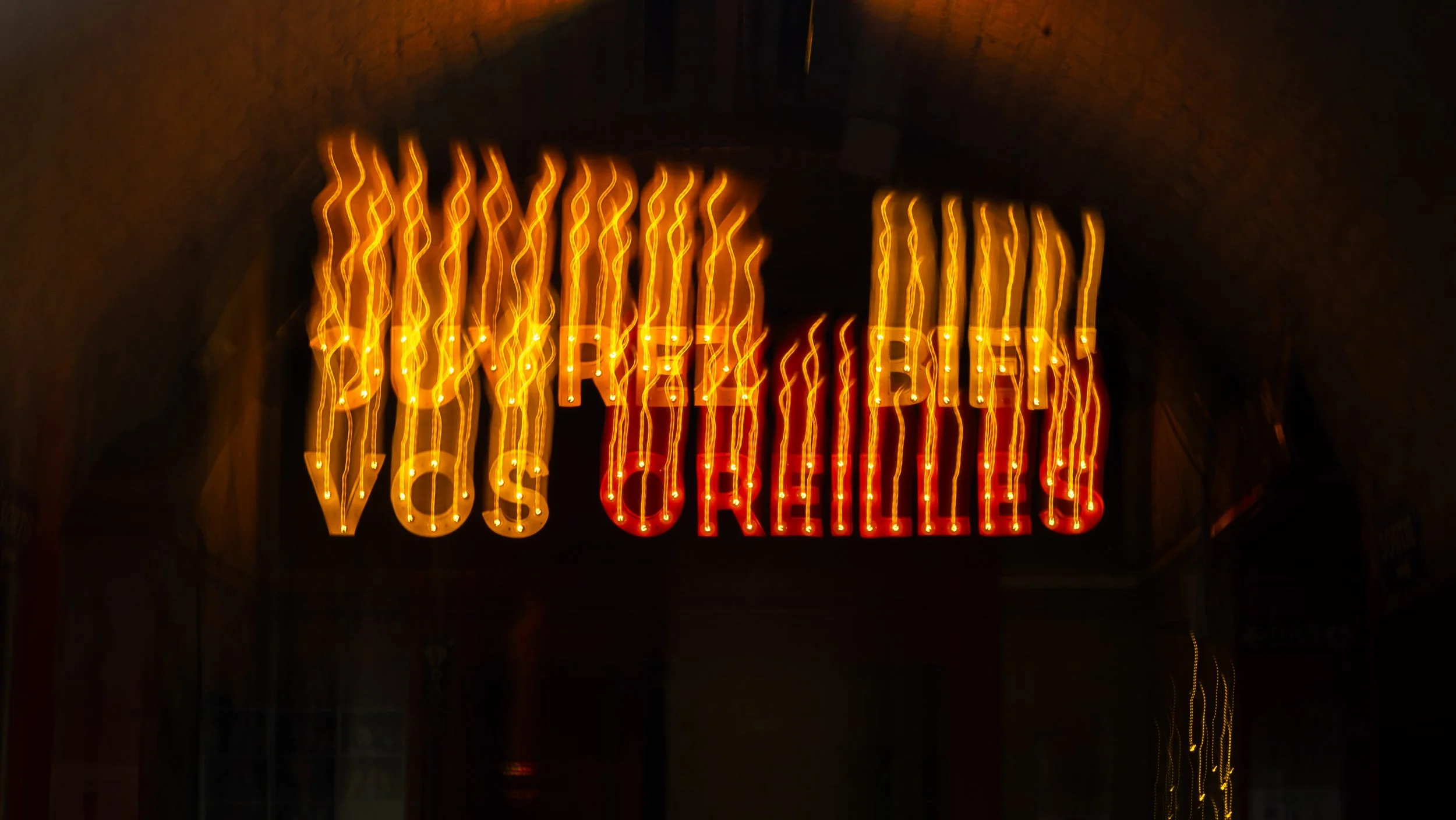 Affiche lumineuse en néon avec un fond noir, affichant partiellement le texte 'VOS OREILLES'.