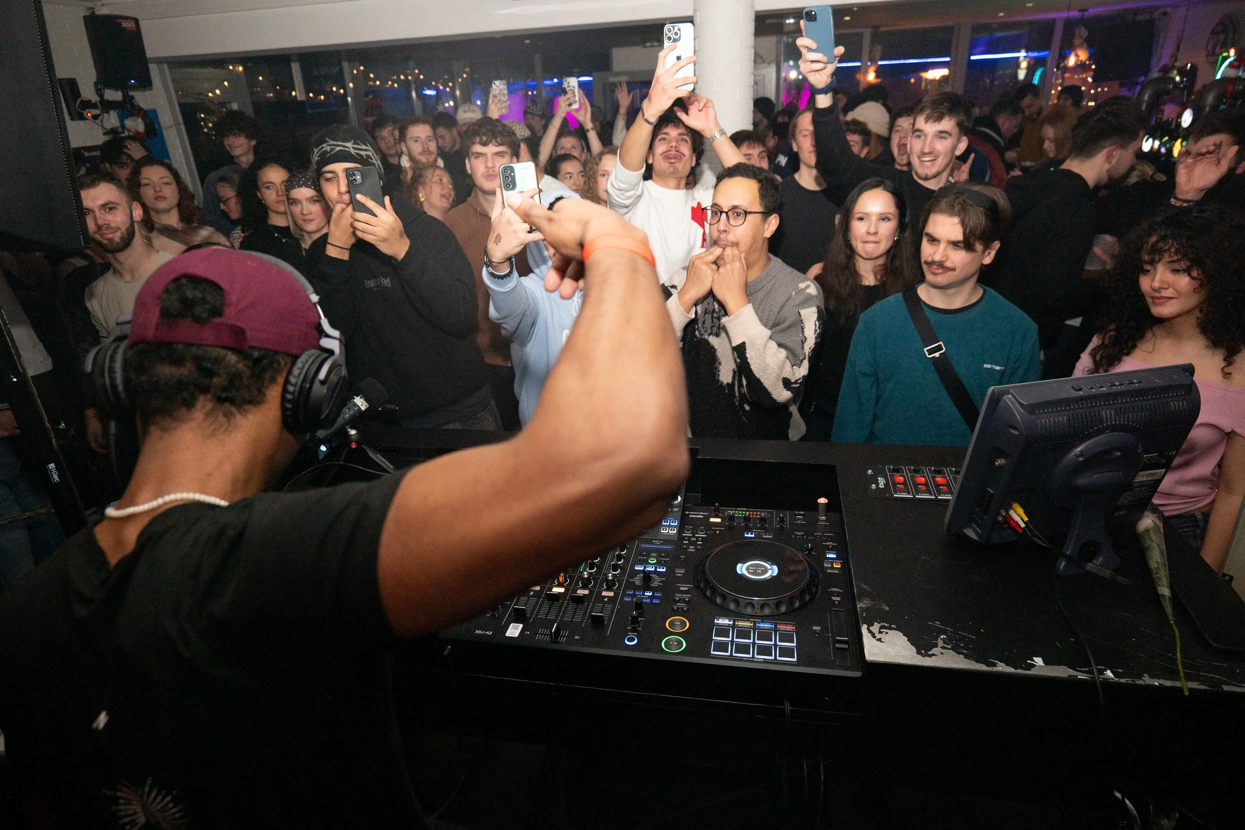 Une foule de jeunes adultes dansant et prenant des selfies lors d'une fête ou d'un concert, avec un DJ en train de jouer de la musique à l'avant.