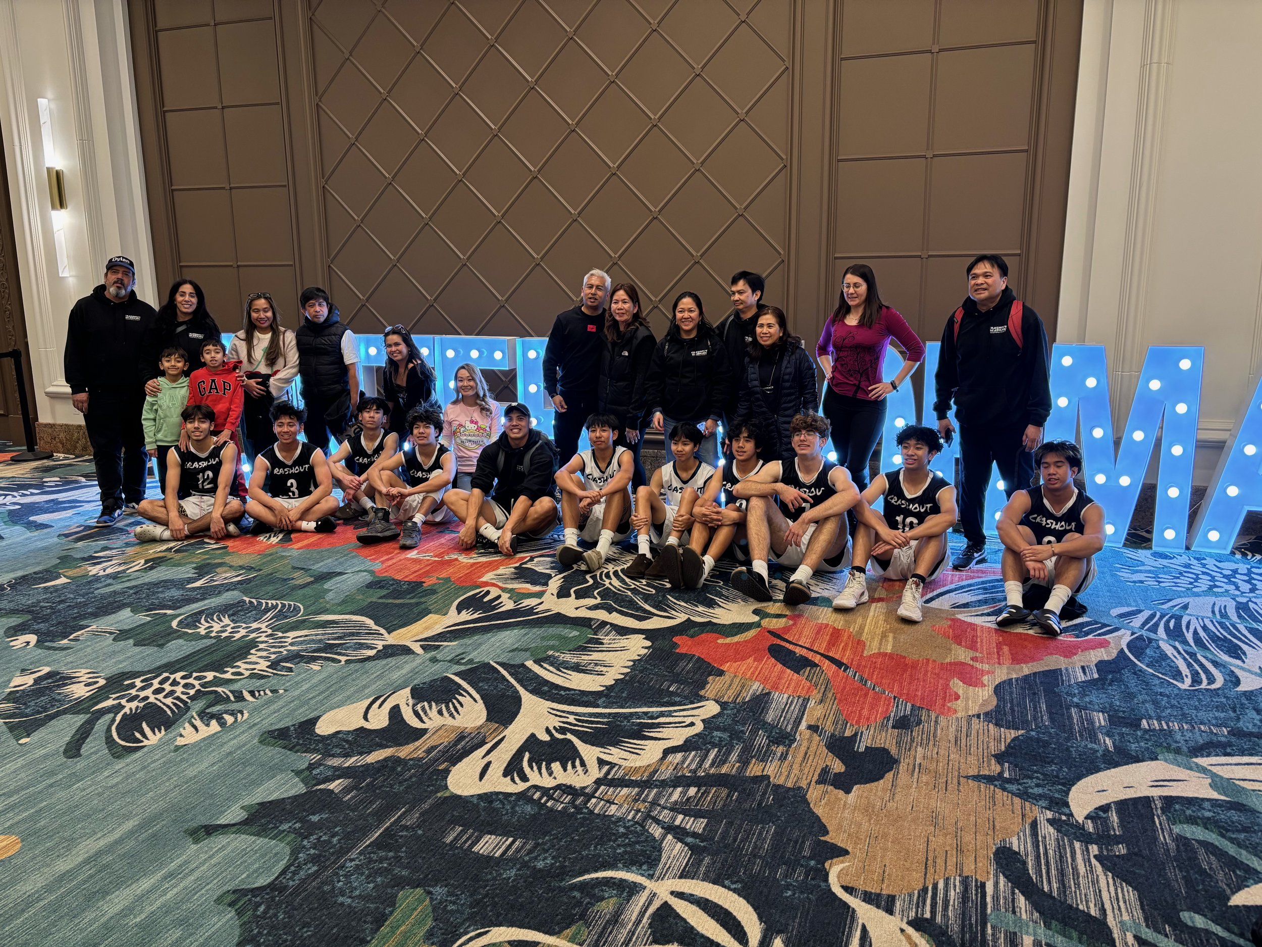 A group of children and adults pose for a photo in front of large illuminated letters spelling out 'DREAM' in a hotel or conference center lobby.