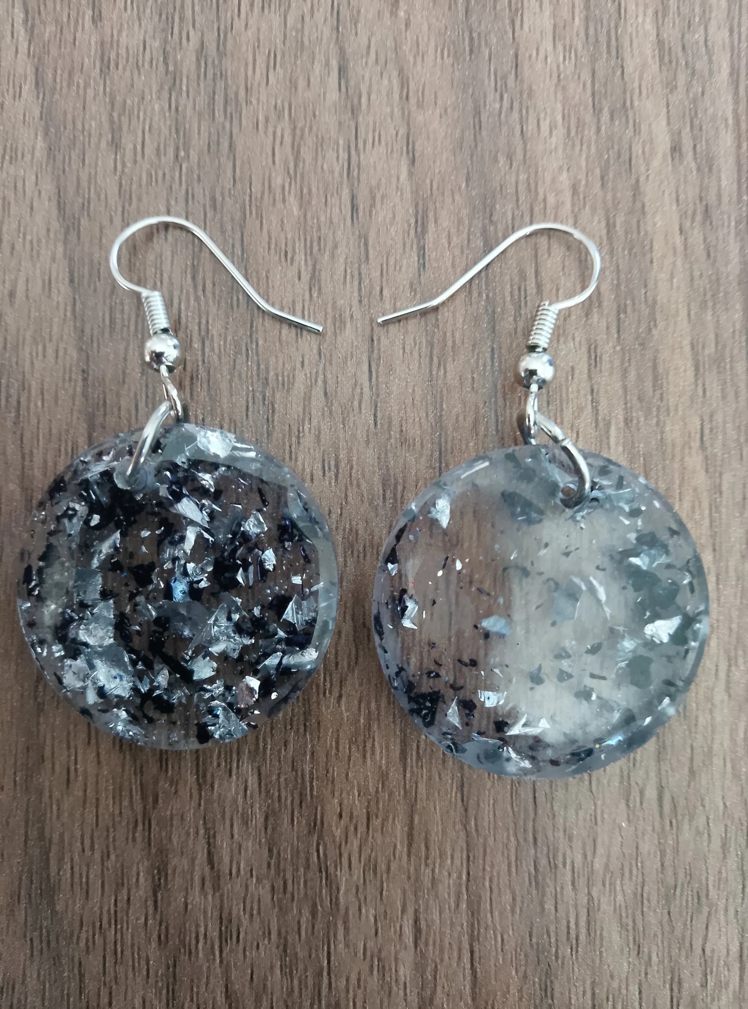 Silver earrings with large, oval-shaped, reflective surfaces and fishhook-style clasps on a wooden surface.