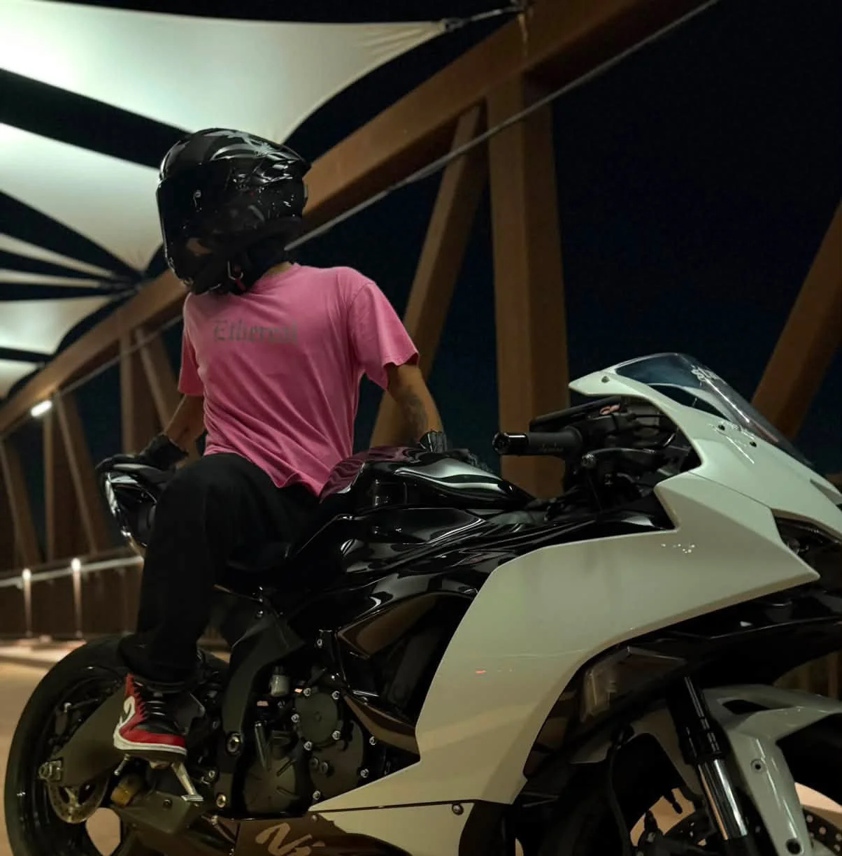 A person wearing a black helmet and pink shirt riding a white and black sport motorcycle in a covered structure at night.