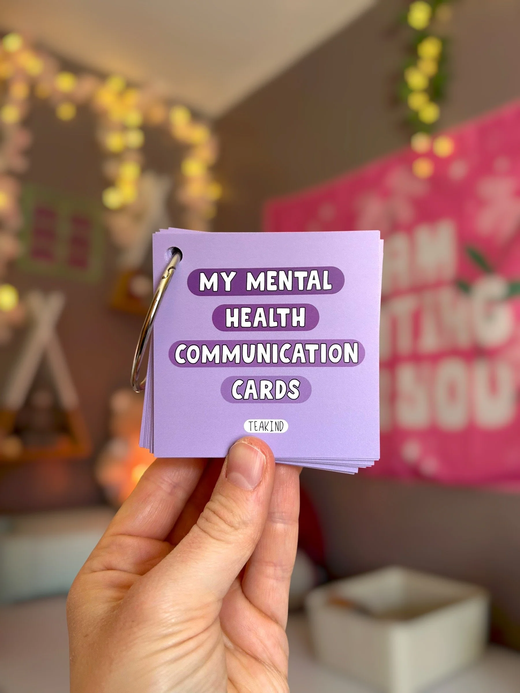 Hand holding a stack of purple mental health communication cards with text, in a store or classroom setting.