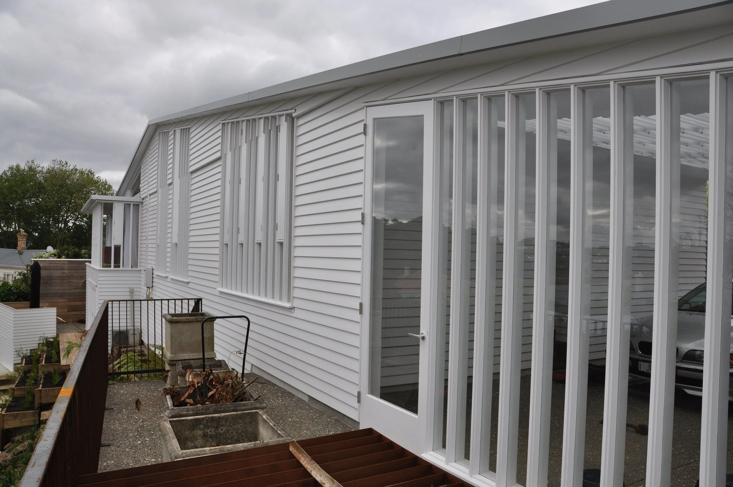 A white house with a large windowed sunroom and a small balcony. The sky is overcast with gray clouds.