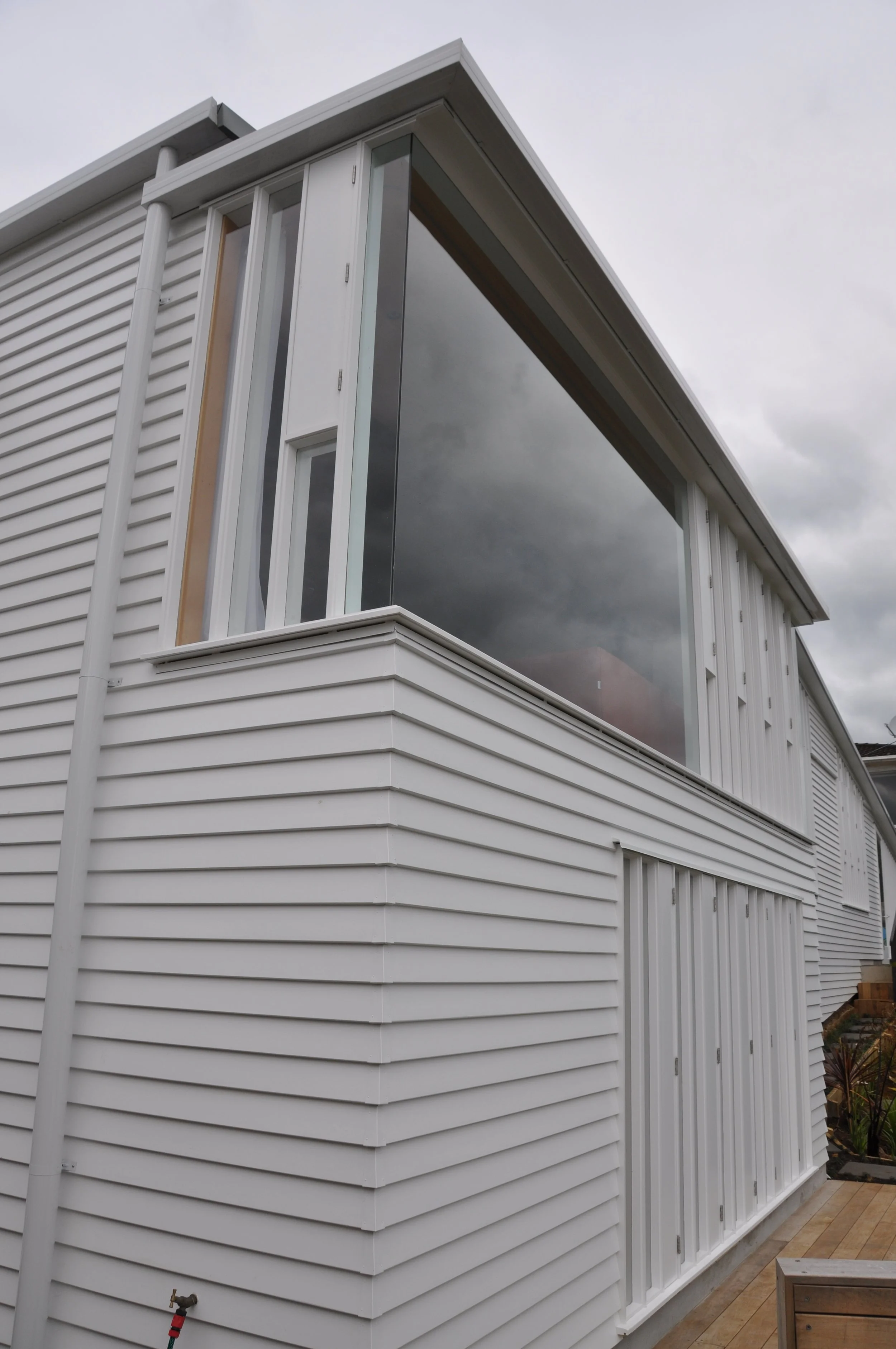 White house exterior with vinyl siding, large windows, and a flat roof, under a cloudy sky.