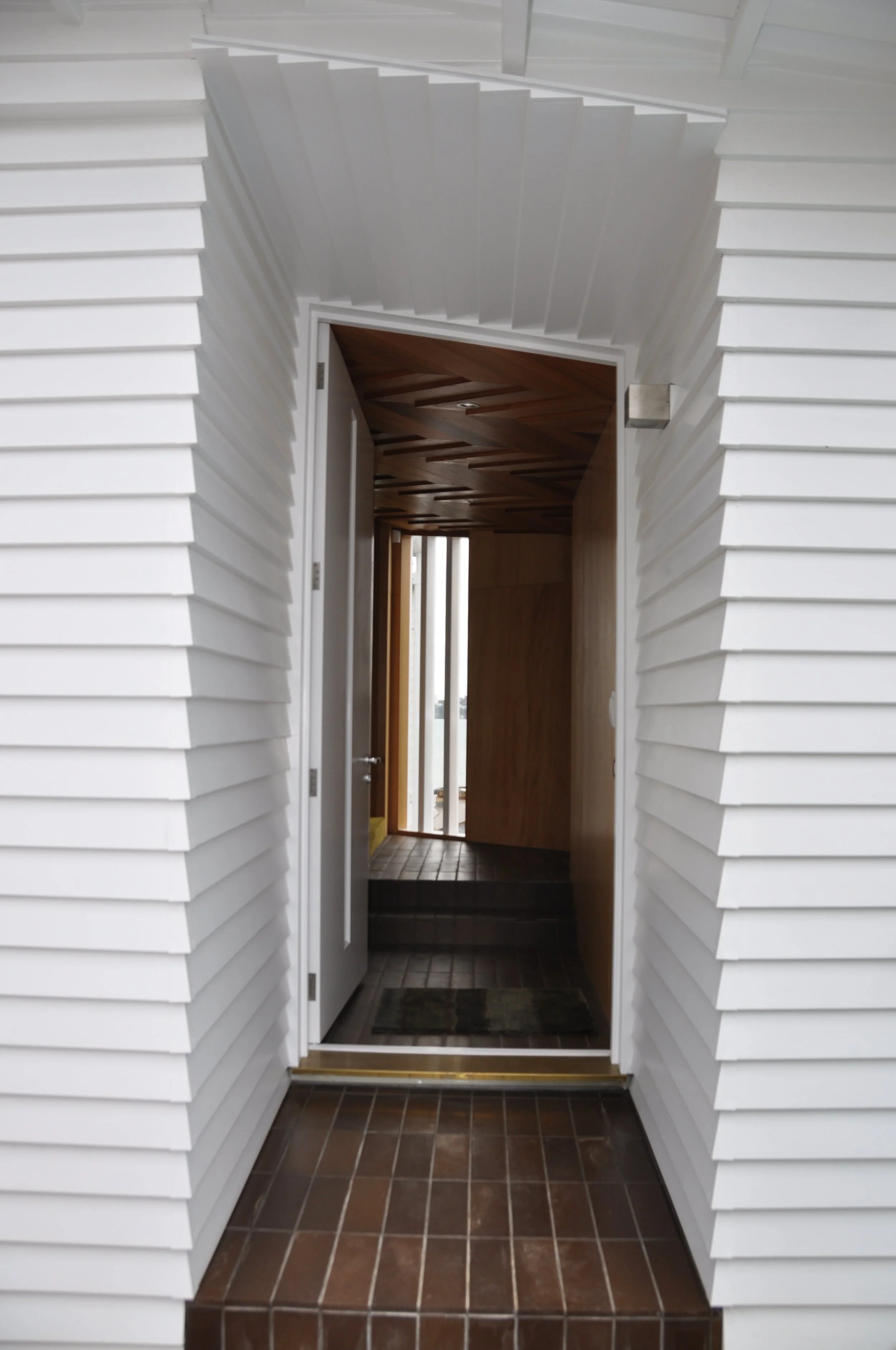 Entryway with a step, brown tiled floor, white siding walls, and a wooden door with glass window panes.