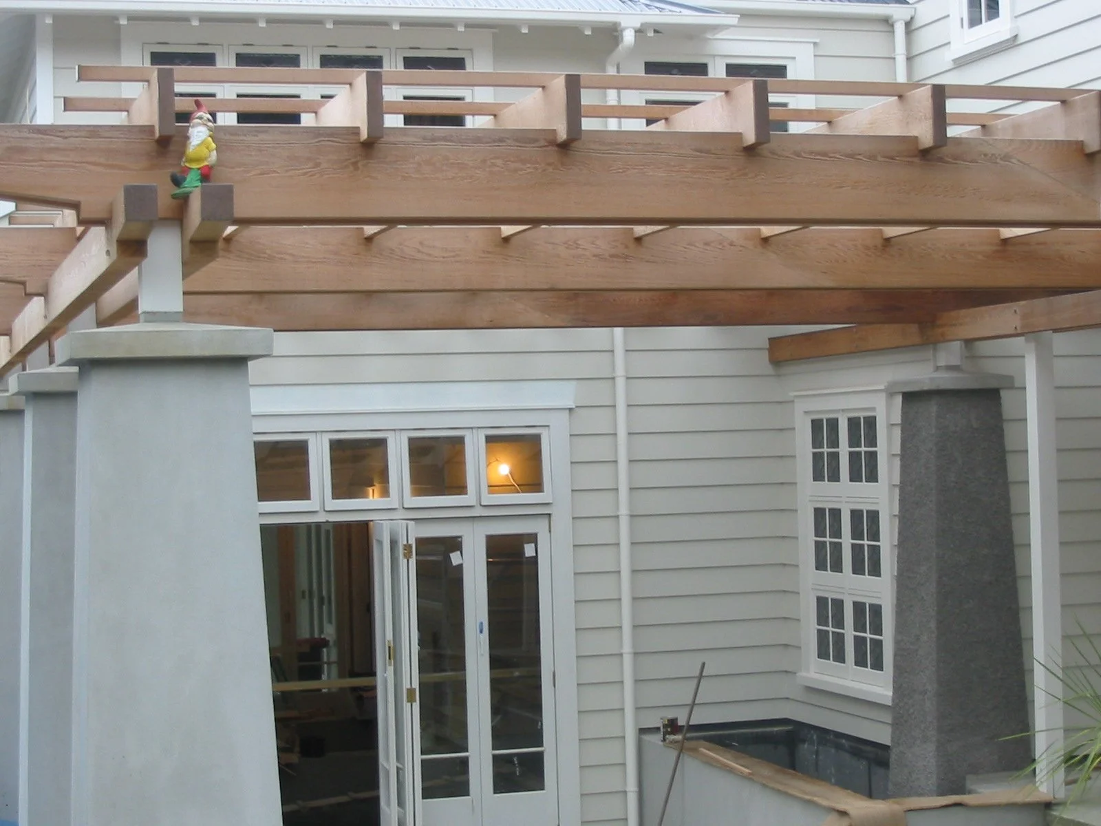 Construction site of an outdoor deck attached to a house, with wooden beams and columns, a sliding glass door, and windows in the background.