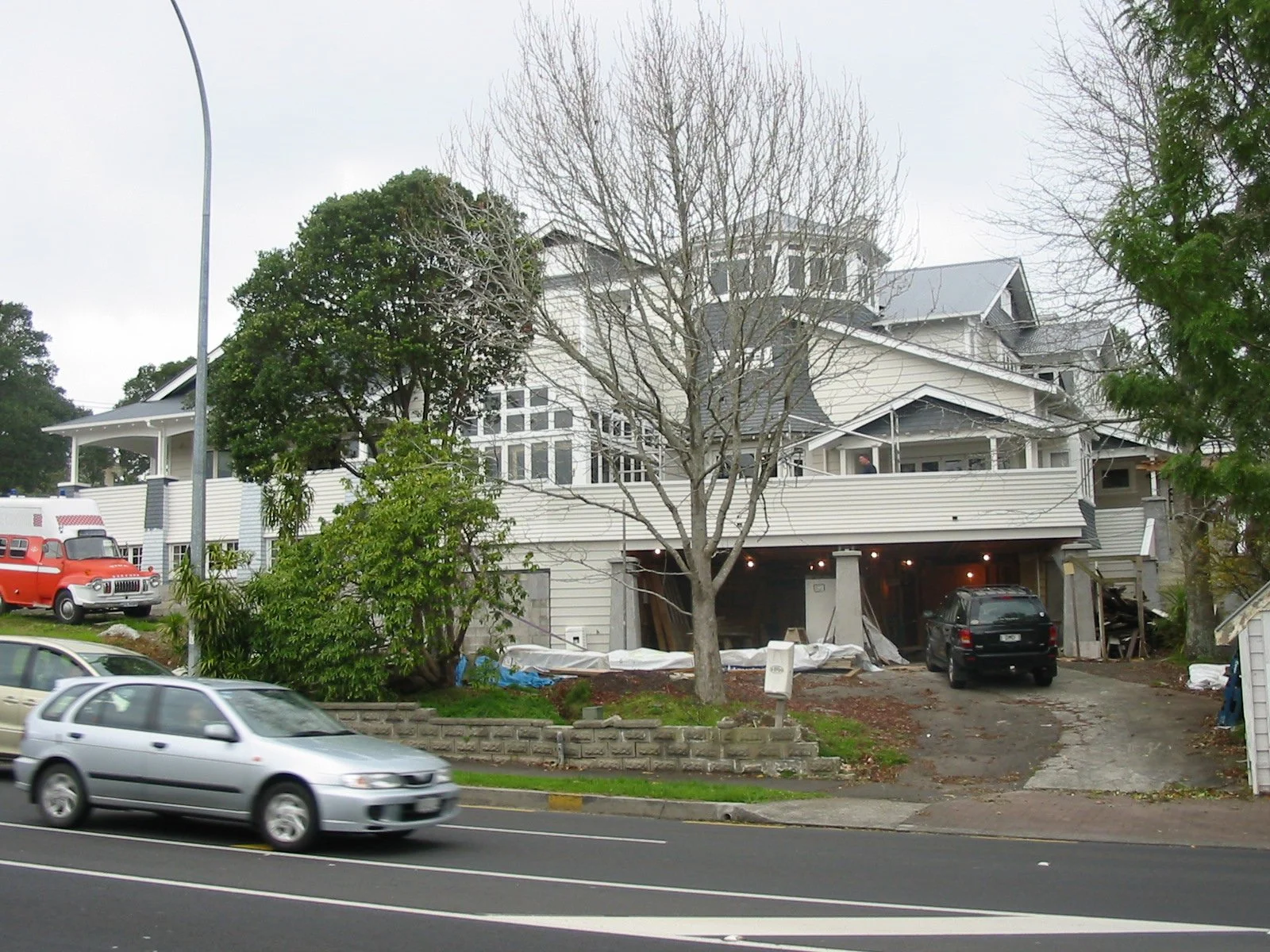 Multi-story house under construction with construction materials and vehicles parked nearby, cars driving on the street in front.