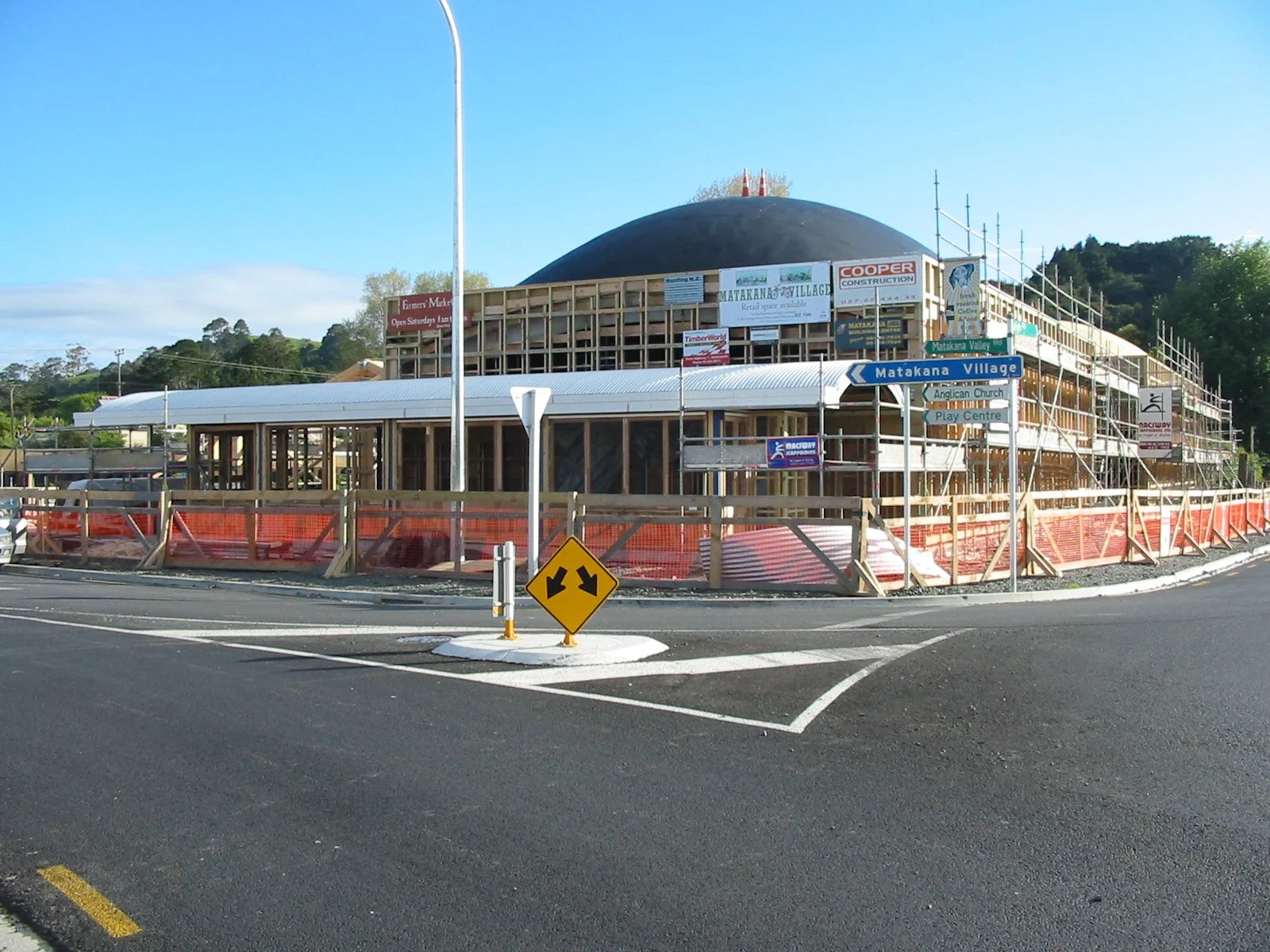 A building under construction with scaffolding and signage, located near a road with directional signs and orange safety barriers.