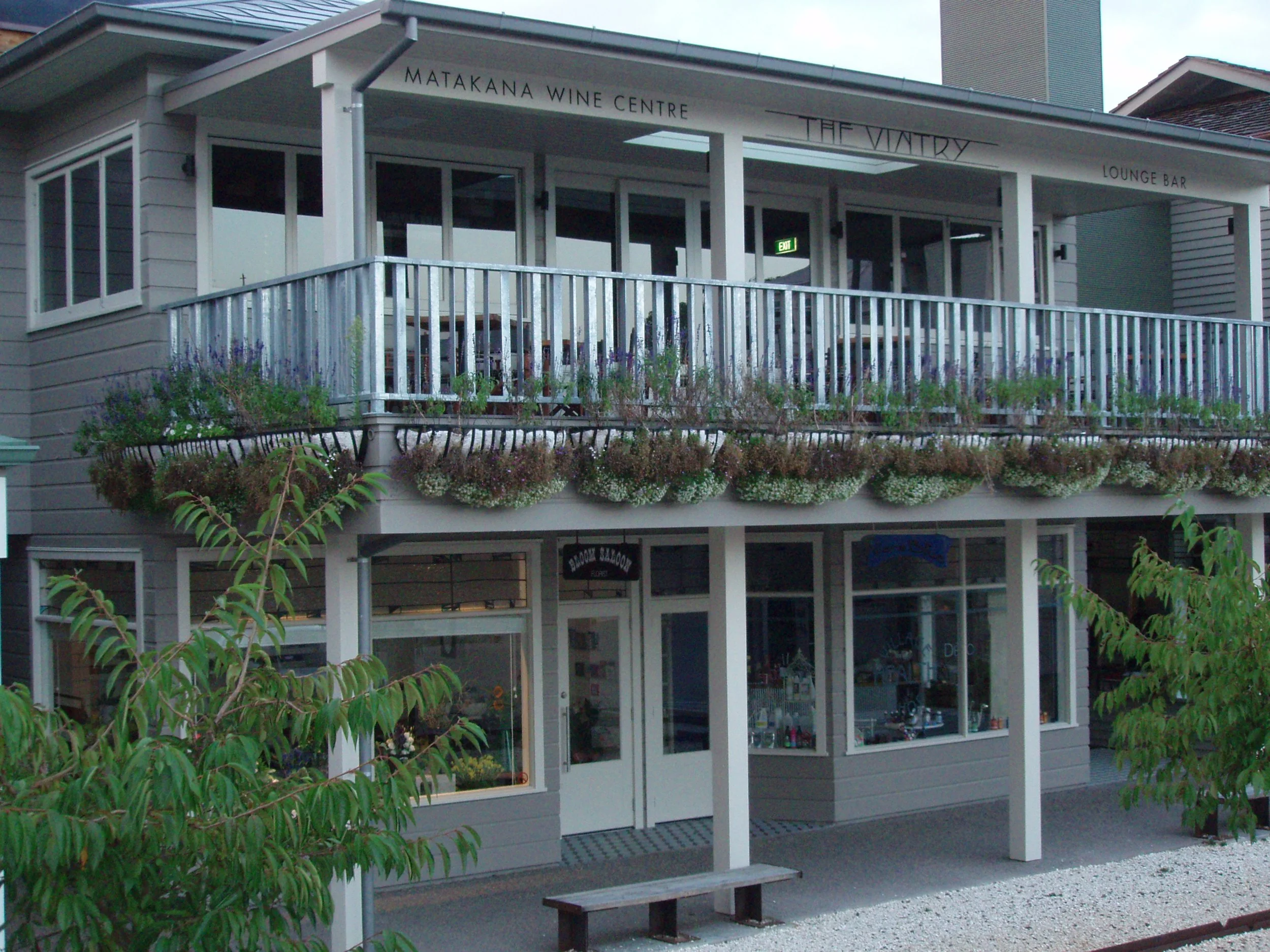 Exterior of Matakana Wine Centre with a balcony, flower boxes, and a lounge bar, surrounded by greenery.