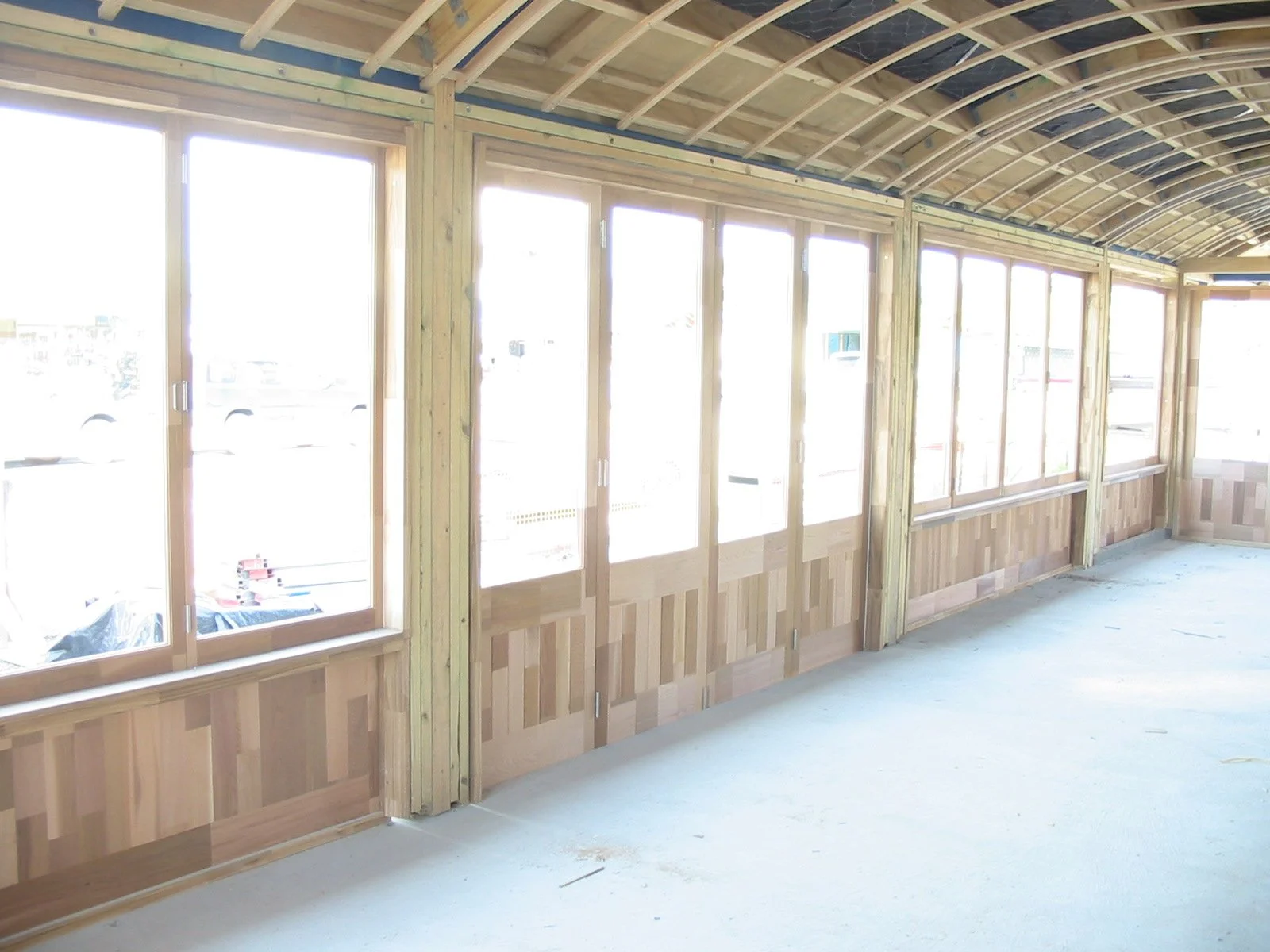 Interior of a room under construction with large windows, wooden framing, and a curved ceiling, with a bare floor.