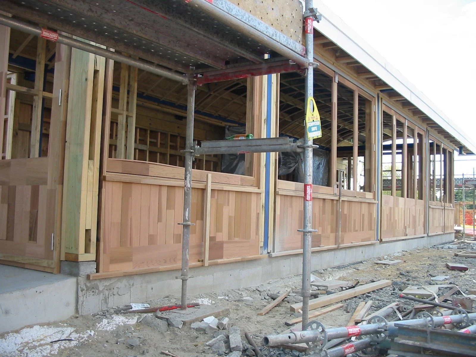 Construction site with a building under construction, showing wooden framing, scaffolding, and construction materials.