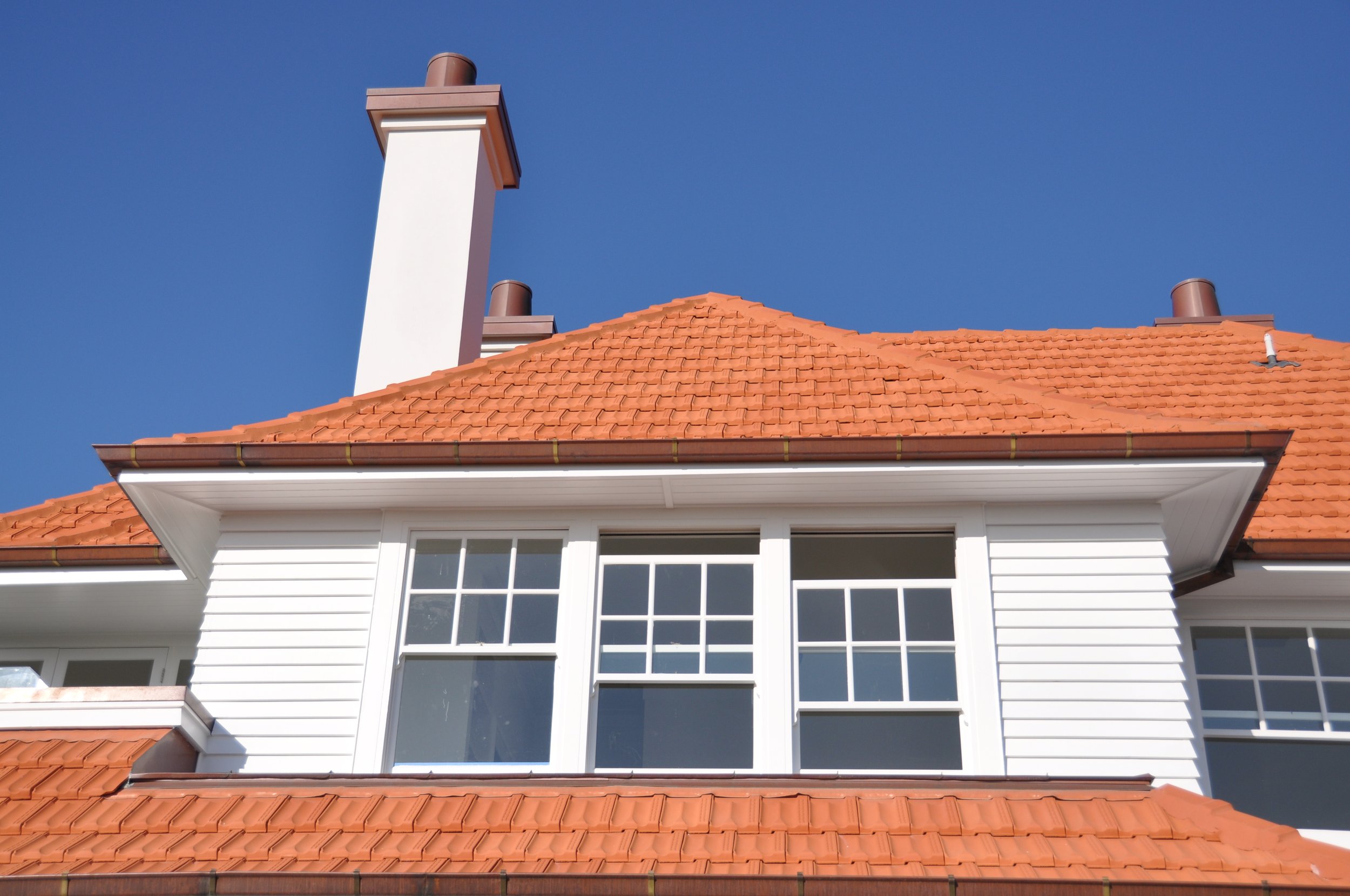 A house with white siding, multiple windows, a red tile roof, and a clear blue sky in the background.