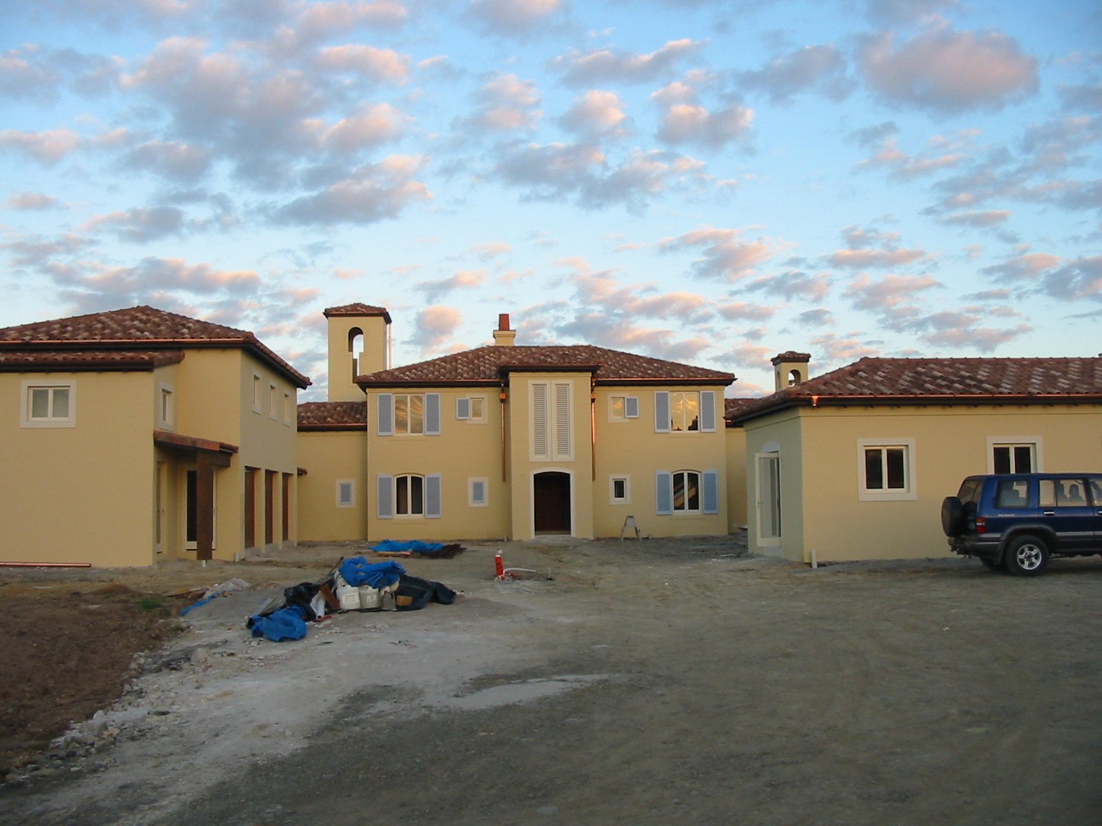 New residential houses under construction with a dirt road in front and a partly cloudy sky at sunset.