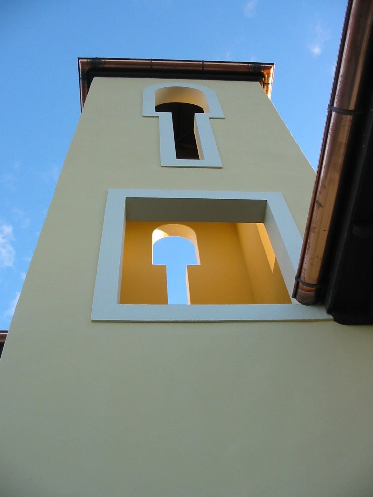 A yellow building with two square-shaped openings featuring a keyhole design, viewed from below against a blue sky.