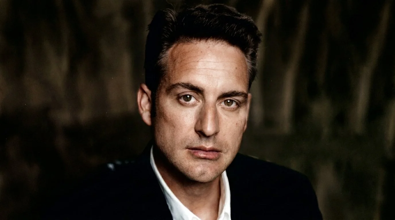 Colin Bloudoff, owner of Steam Boat Productions, close-up portrait of a man with dark hair, wearing a dark jacket and a white shirt, looking directly at the camera with a neutral expression.