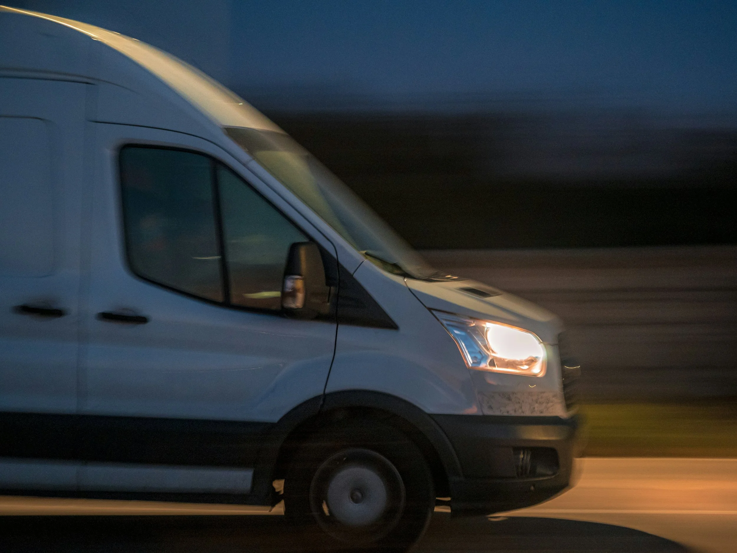 A white van driving on the road during dusk or dawn.