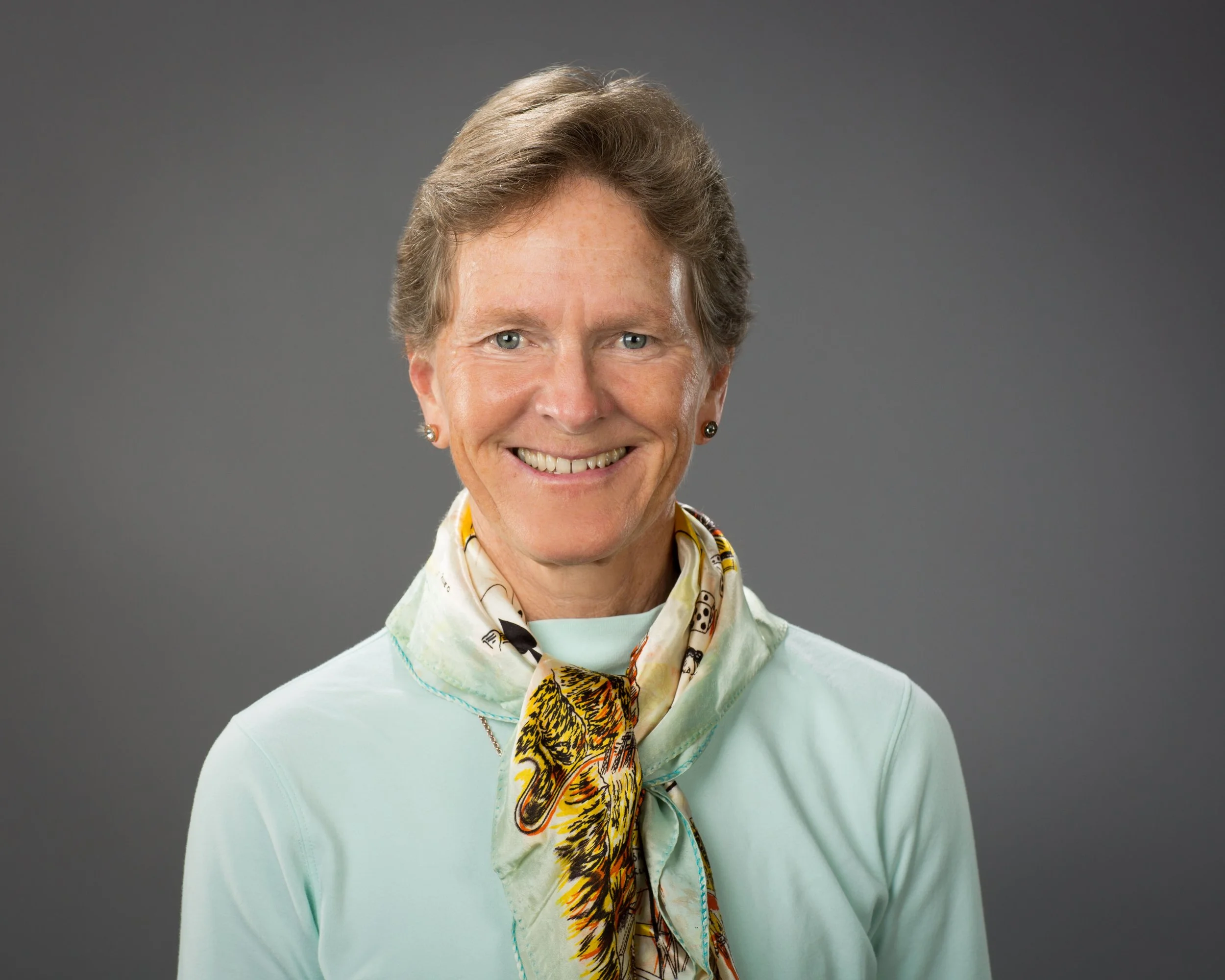 Rae Raptor wearing a light-colored cardigan and a scarf with a tiger design, posing against a plain gray background.