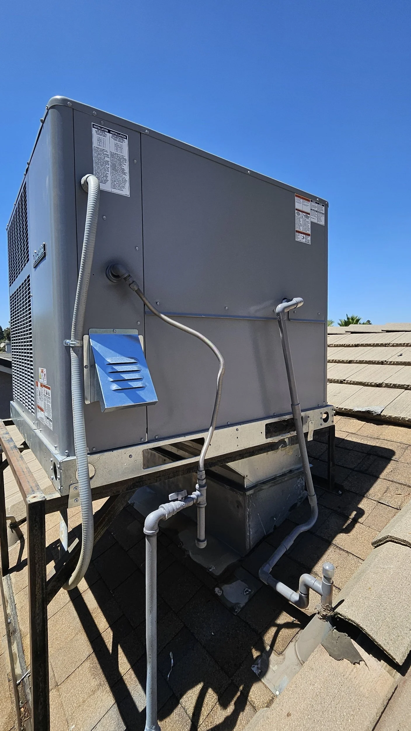 A rooftop HVAC unit installed on a shingled roof against a clear blue sky.