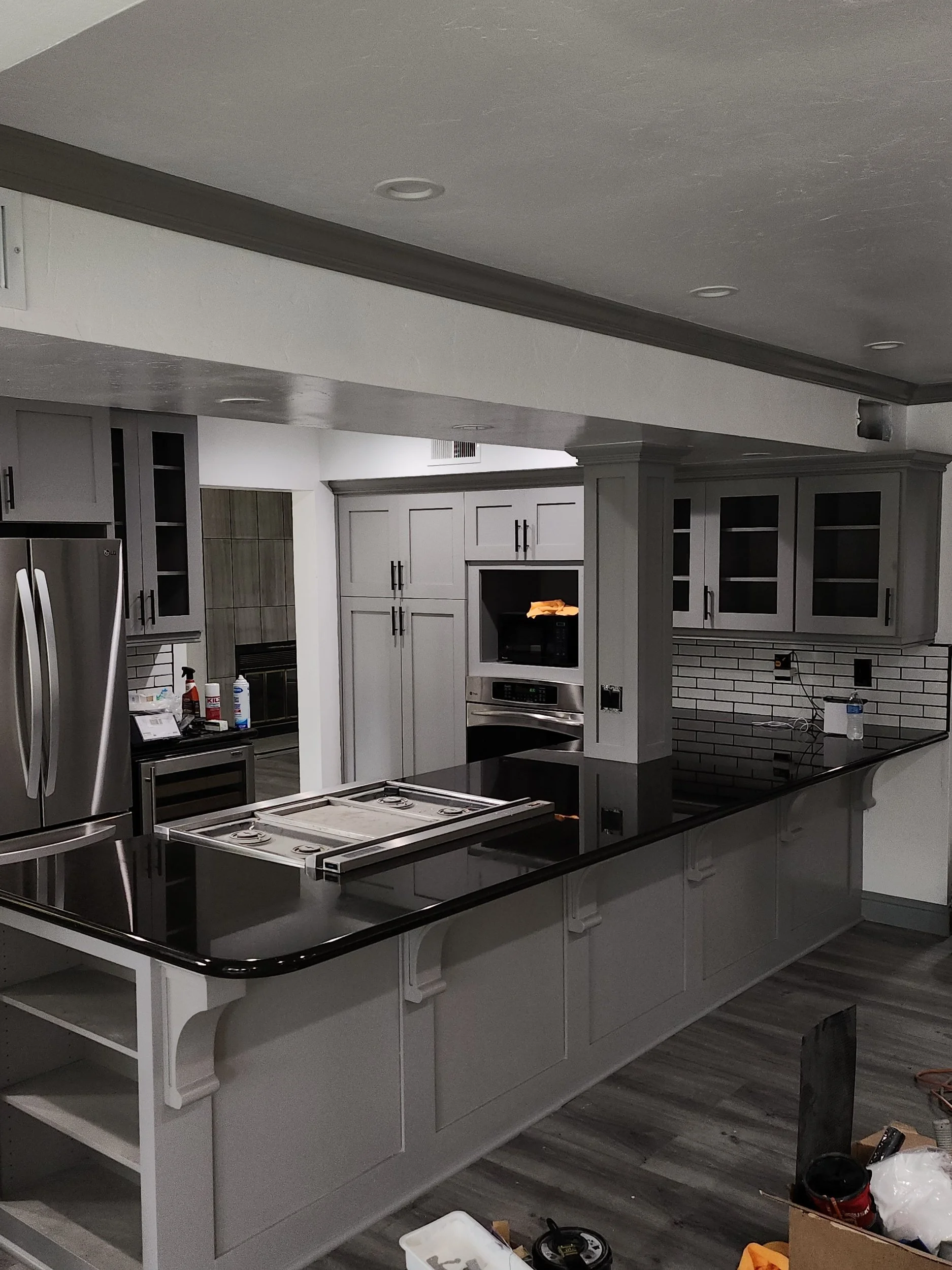 A kitchen under renovation with gray cabinets, a black countertop, a white kitchen island with a black counter, visible tools, and partially installed fixtures.
