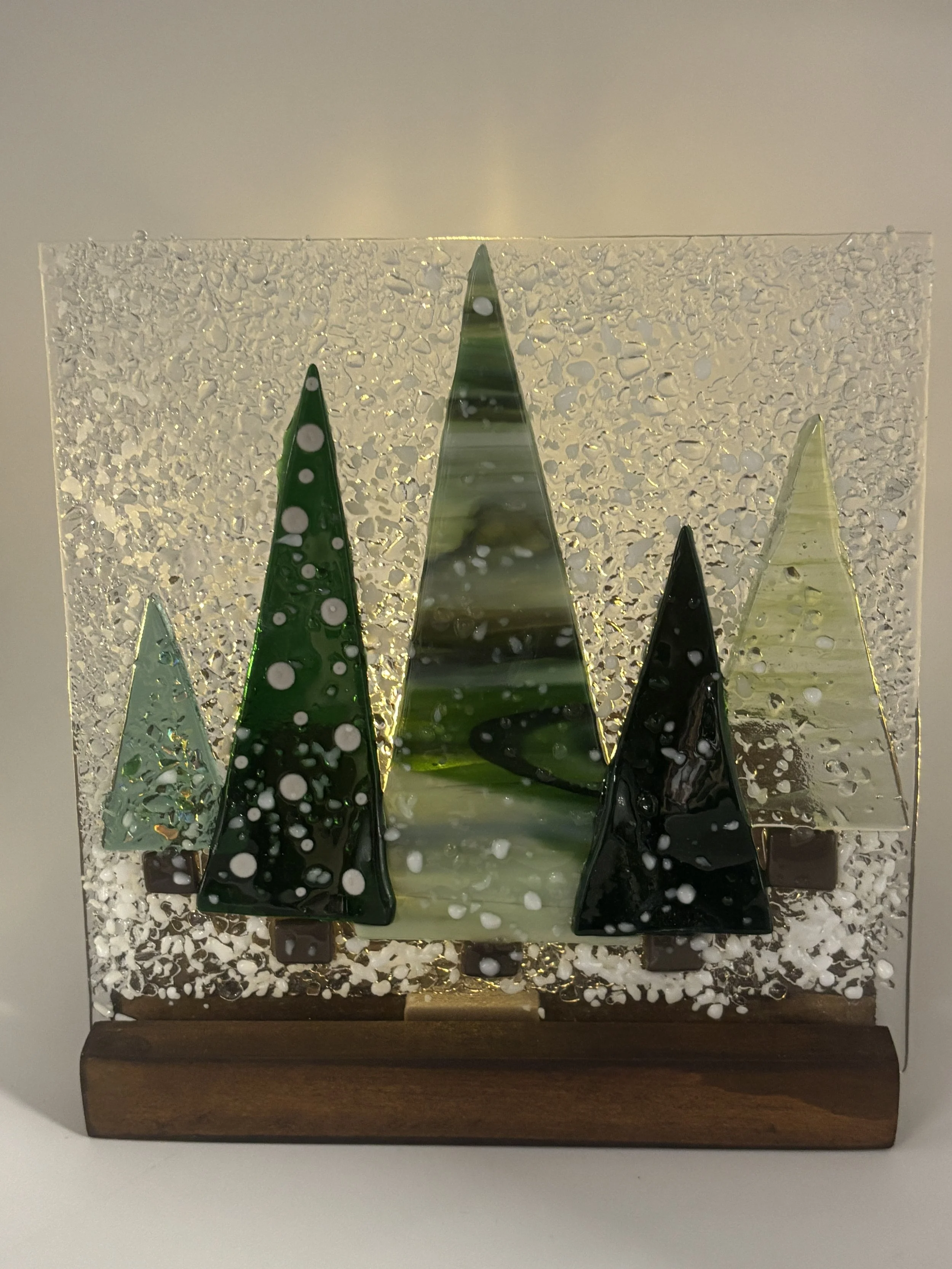 Decorative glass art featuring green and black glass trees on a wooden base with textured glass background and white accents.